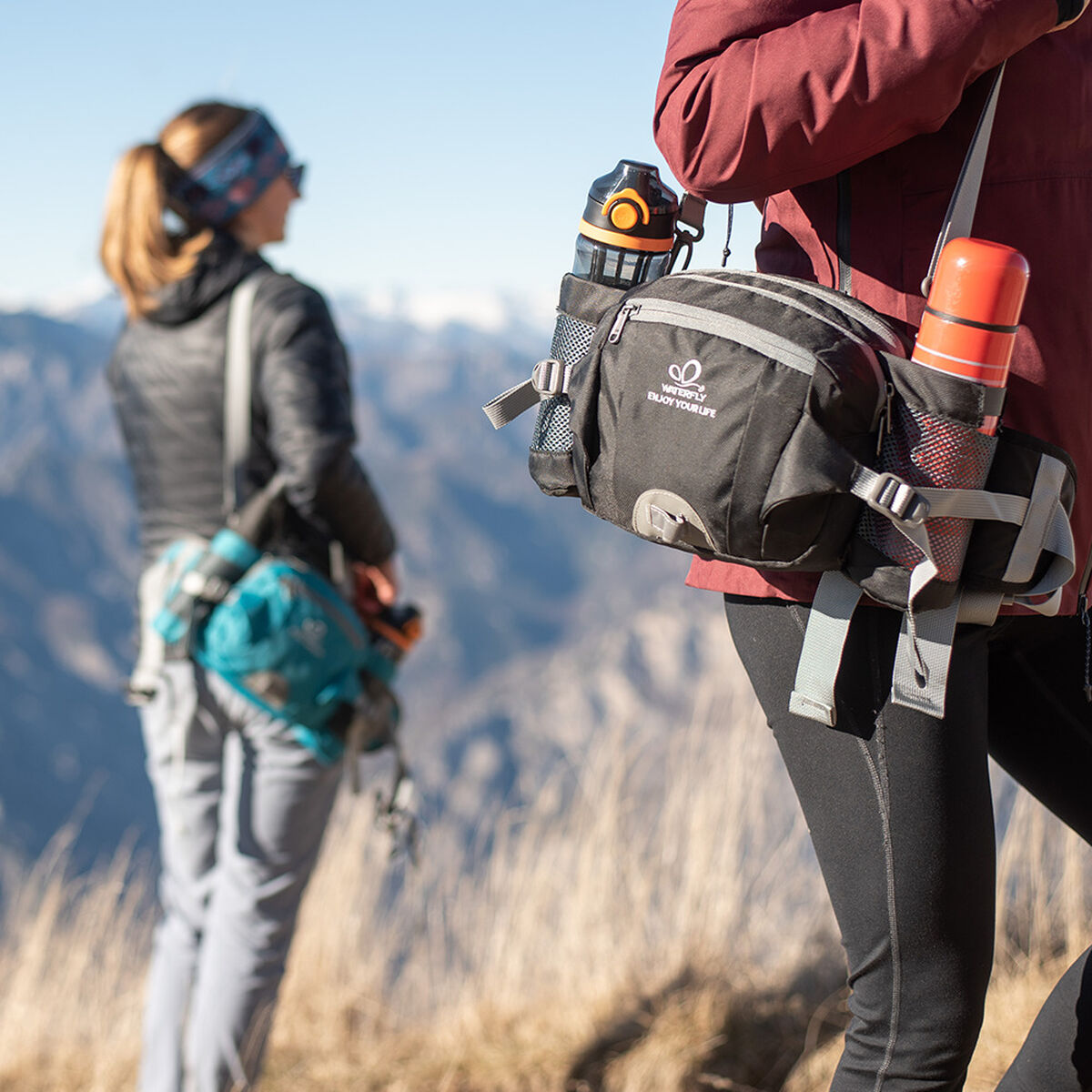 Dos personas caminando por un sendero de montaña con una persona usando una riñonera negra.