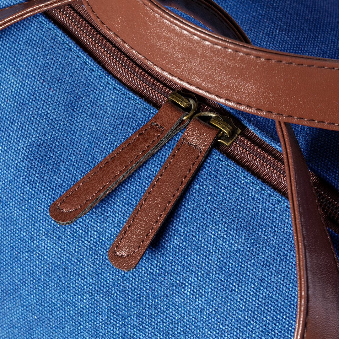 Primer plano de una bolsa de lona azul con tiradores de cremallera de cuero marrón. Cremalleras abiertas.