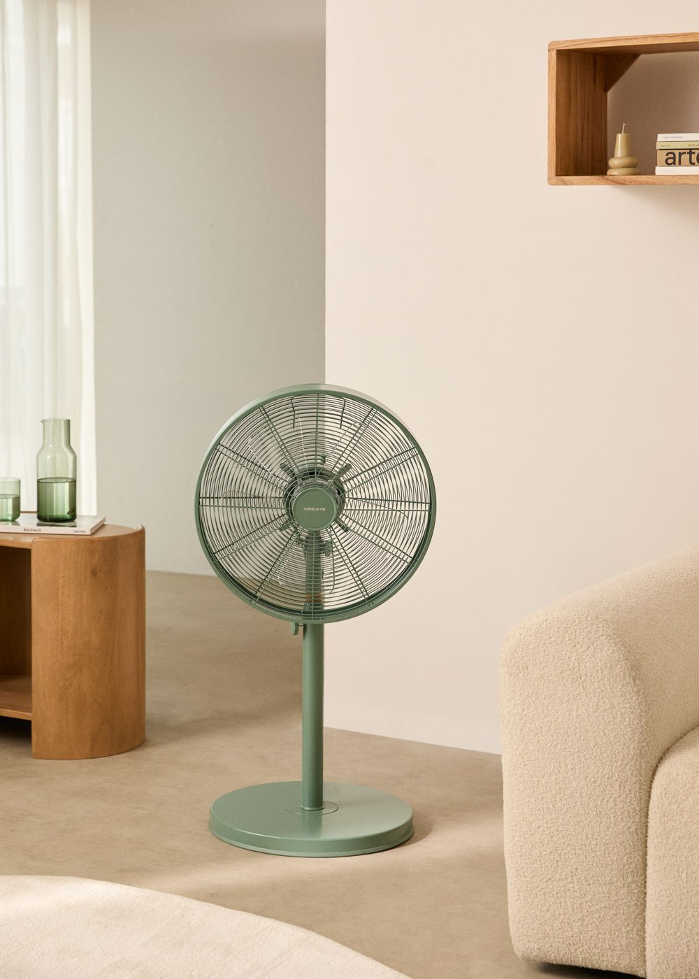 Ventilador de pie verde en una habitación. El ventilador está frente a una pared y una mesa.