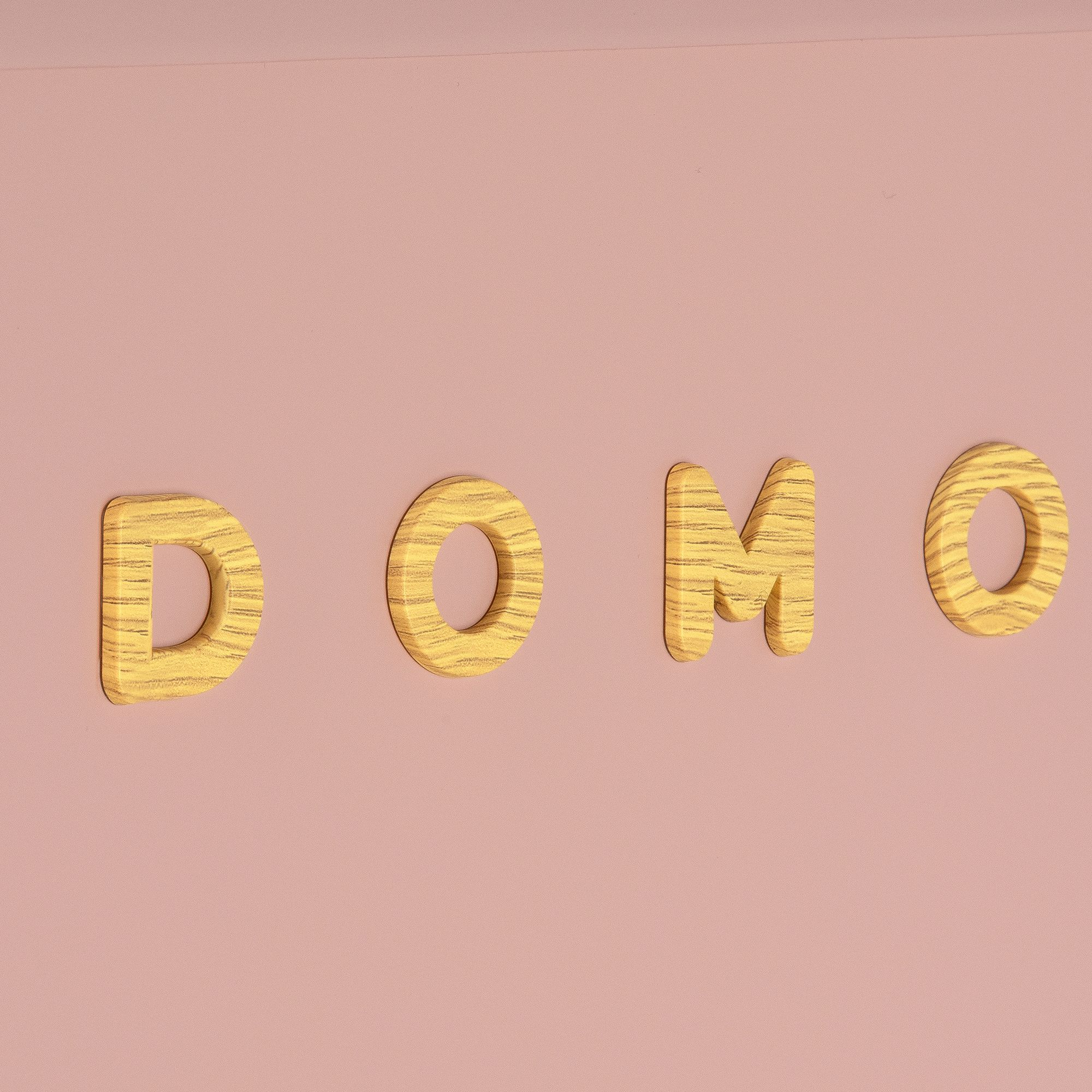 La parola 'DOMO' in lettere di legno su sfondo rosa. Le lettere hanno un aspetto venato.
