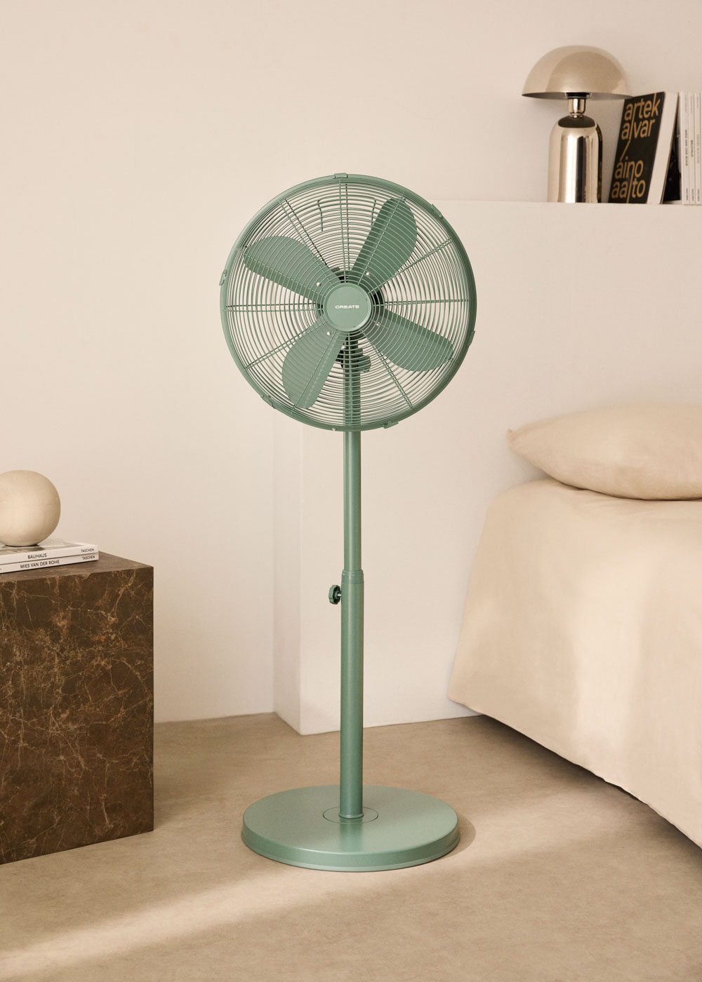 Ventilador verde, paredes beige, cama y mesa auxiliar con objetos.