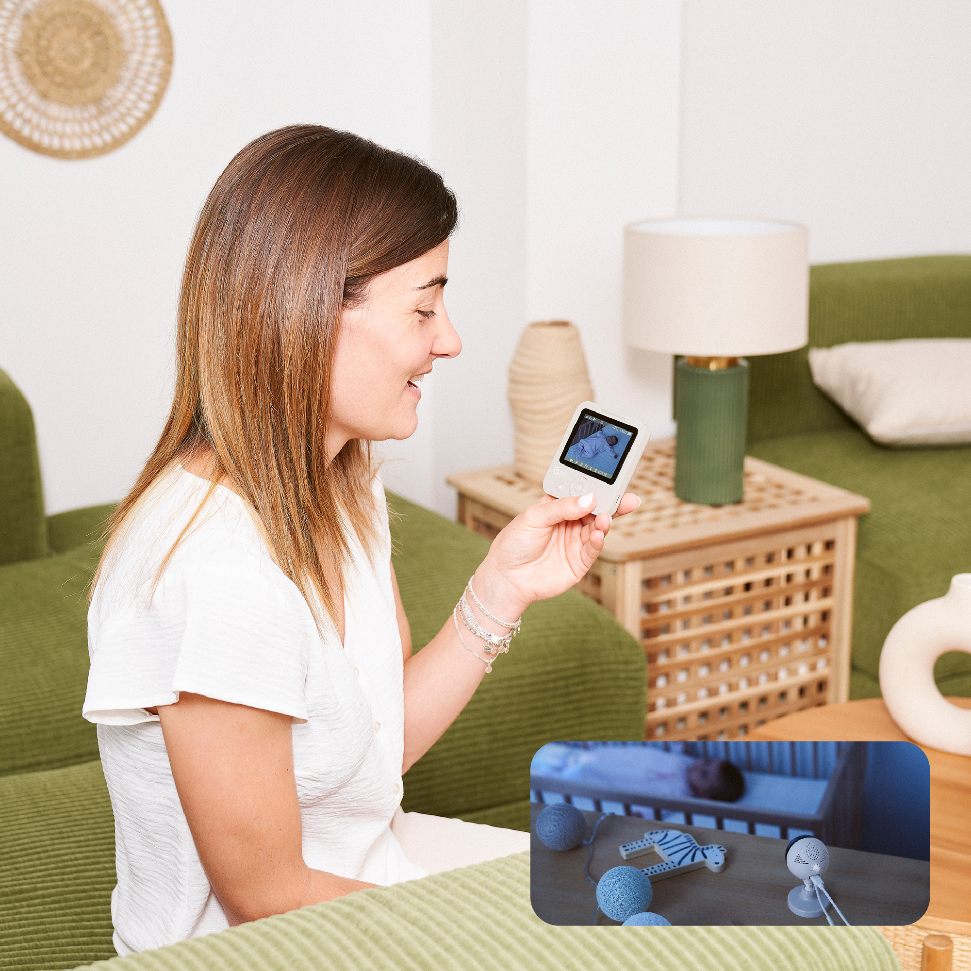 Frau hält einen Baby Monitor, lächelt. Ein kleiner Bildschirm zeigt ein Baby im Bettchen.