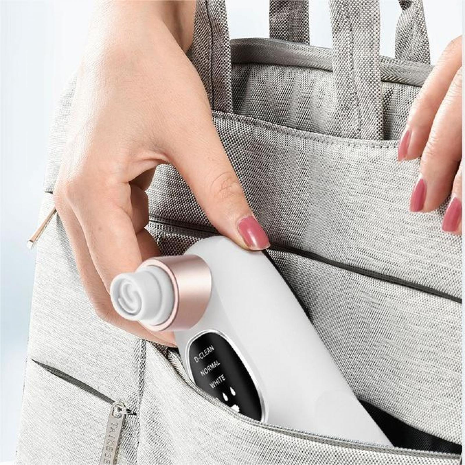 Hand, die ein weißes und roségoldenes Hautpflegegerät in einer grauen Tasche hält.