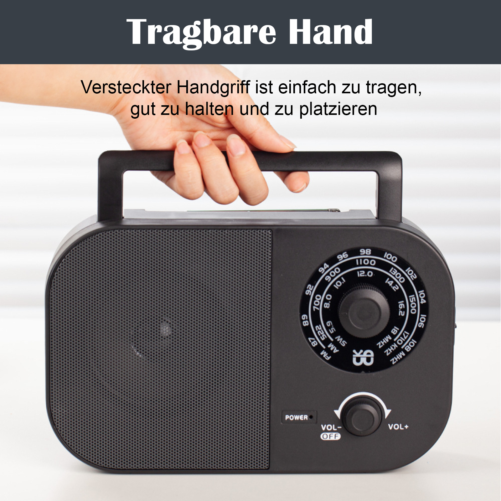 Ein schwarzes Radio mit Griff. Eine Hand hält den Griff. Das Radio steht auf weißer Fläche.