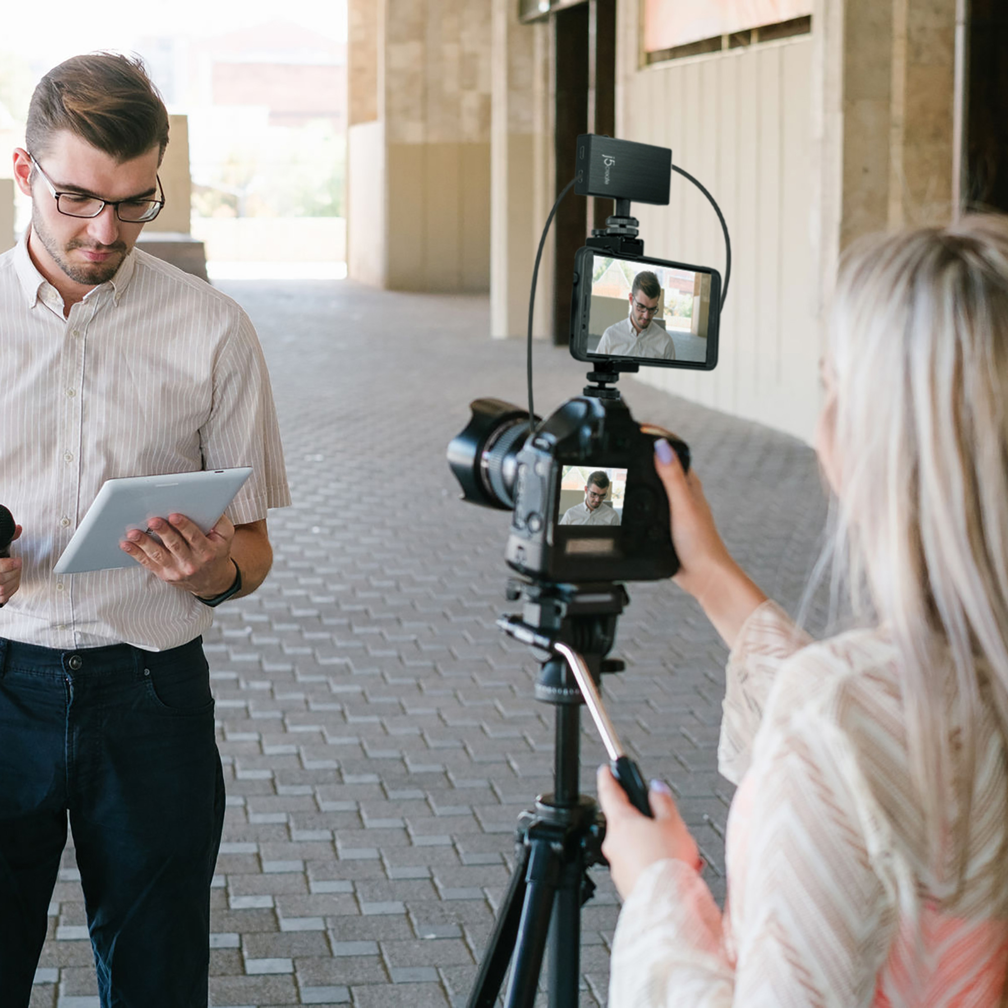 Mężczyzna w okularach trzymający tablet i kobieta filmująca go kamerą. Kamera jest na statywie.