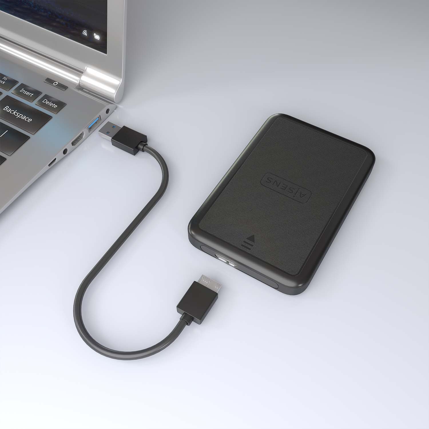 Laptop collegato a un disco rigido esterno nero. Sfondo bianco.