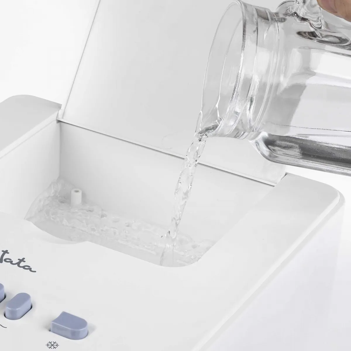 Una jarra de vidrio vierte agua en un enfriador de aire blanco. El enfriador tiene botones y un recipiente de agua.
