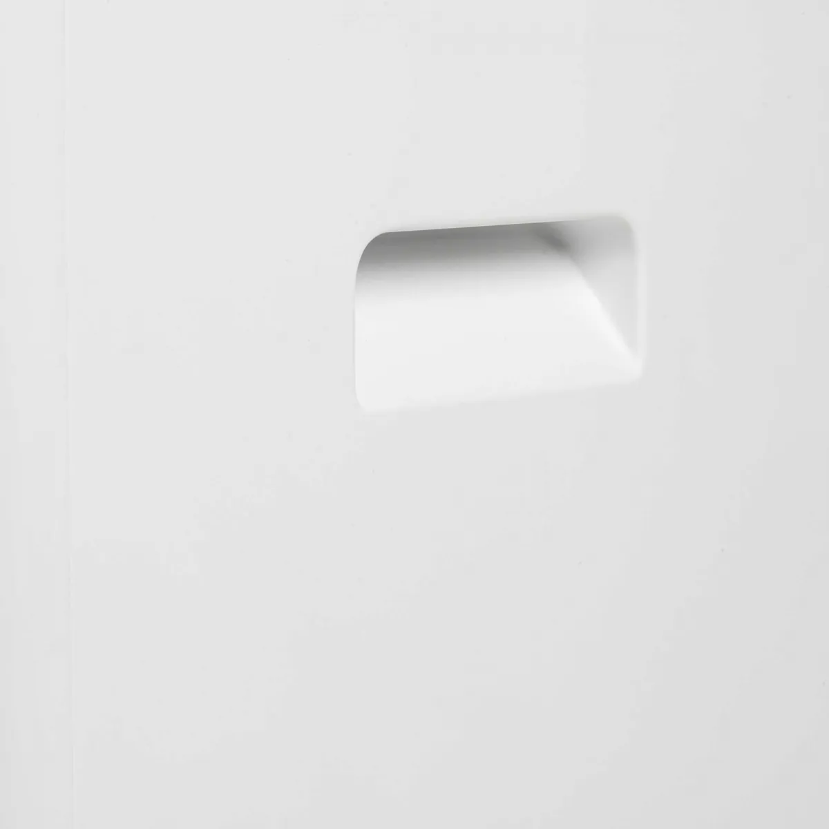 Primer plano de una superficie blanca con una manija rectangular empotrada. La manija está centrada.