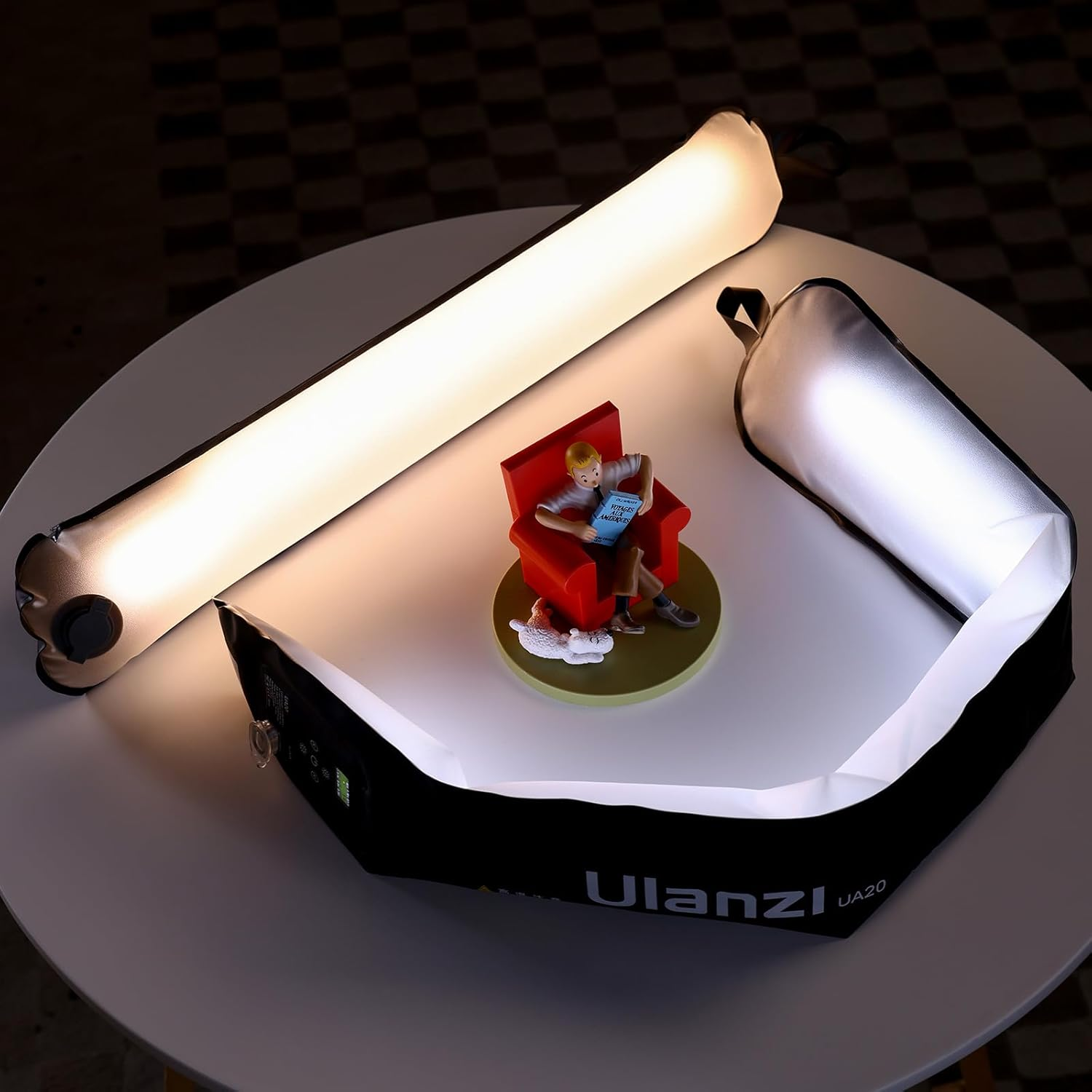 Una figura de Tintín en una silla roja, con luces en una mesa. Un perro blanco está a los pies de Tintín. El fondo es a cuadros.