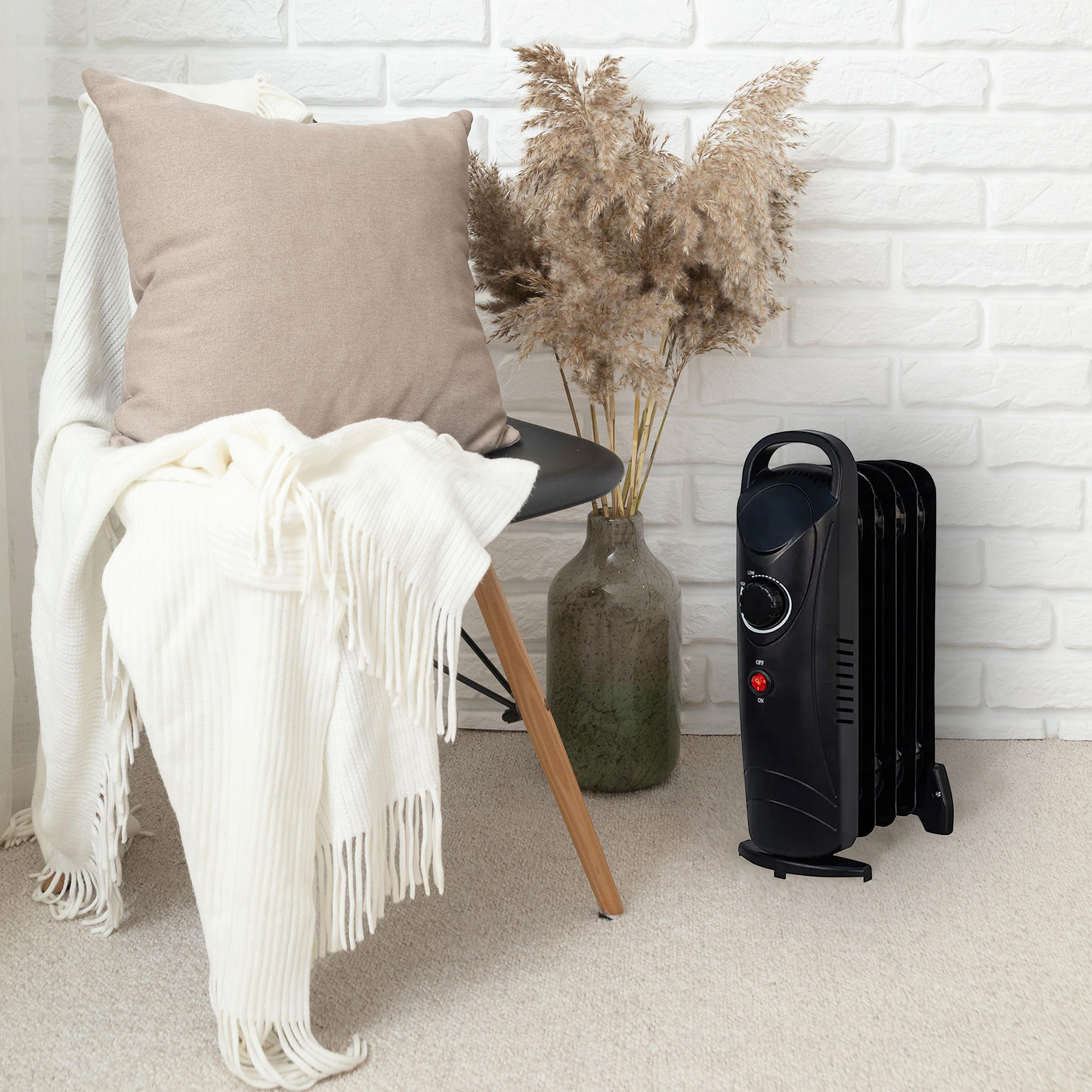 Ein schwarzer Ölradiator steht neben einem Stuhl mit Decke und Kissen. Weißer Backsteinhintergrund.