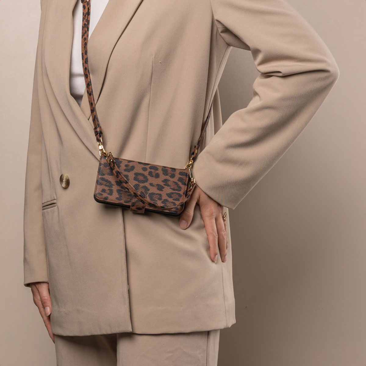 Vrouw in een beige pak, met een telefoonhoesje met een luipaardprint riem.