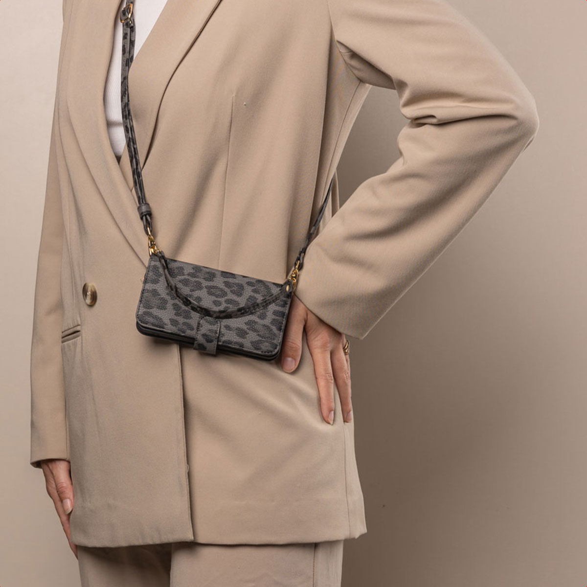 Une femme porte un blazer beige et porte une coque de téléphone à imprimé léopard avec une sangle.
