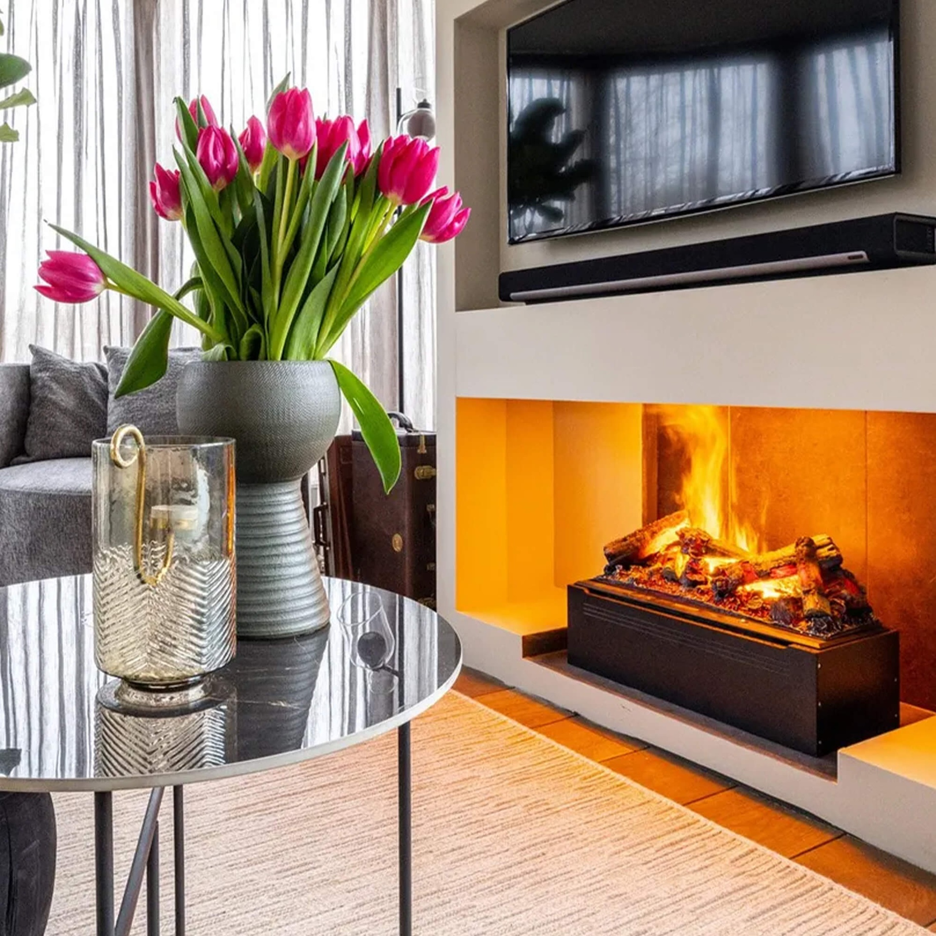 Een moderne woonkamer met een open haard, een tafel met bloemen en een tv.