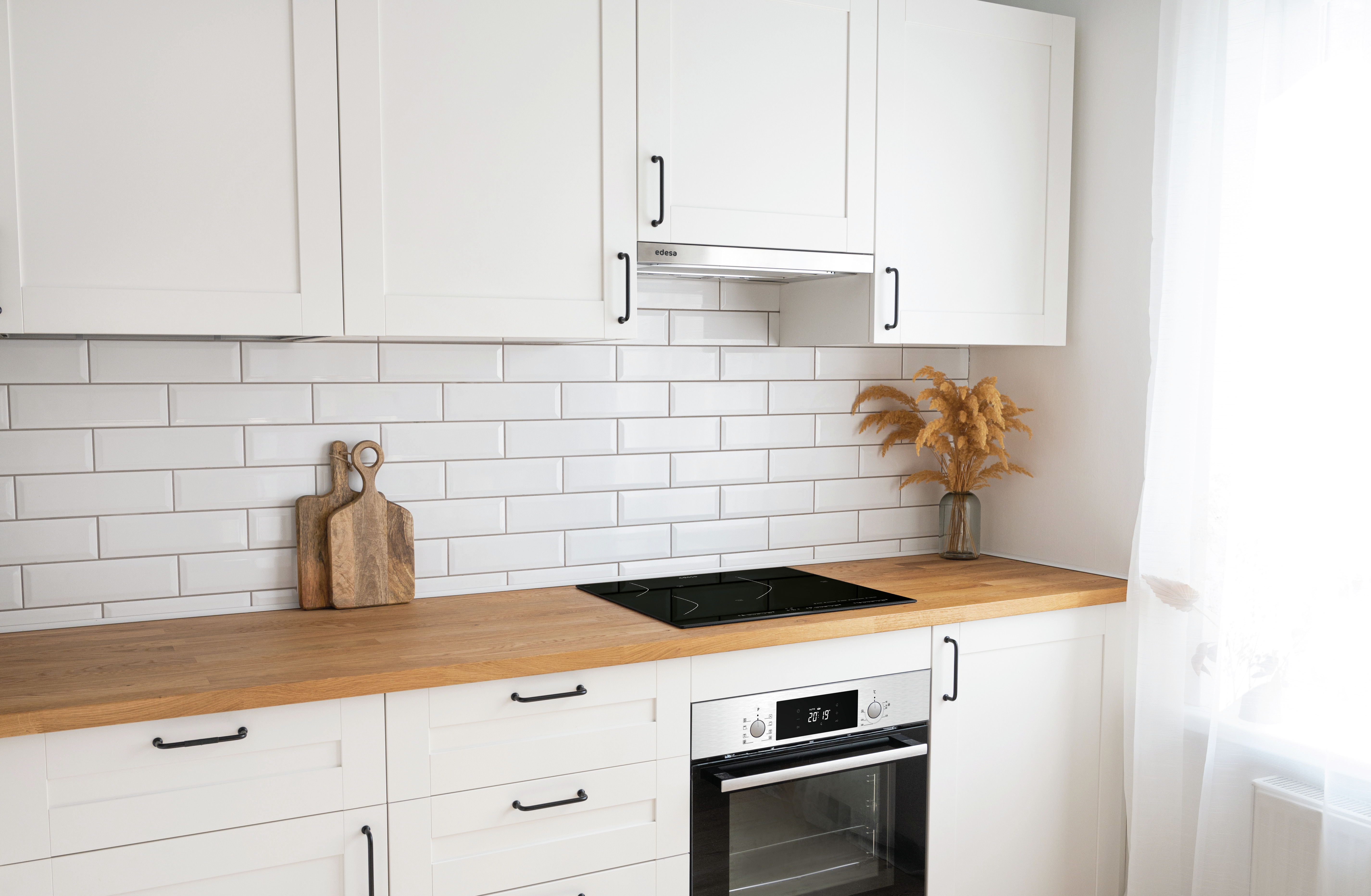 Una cocina con gabinetes blancos, encimera de madera y salpicadero de azulejos blancos. Hay dos tablas de cortar.