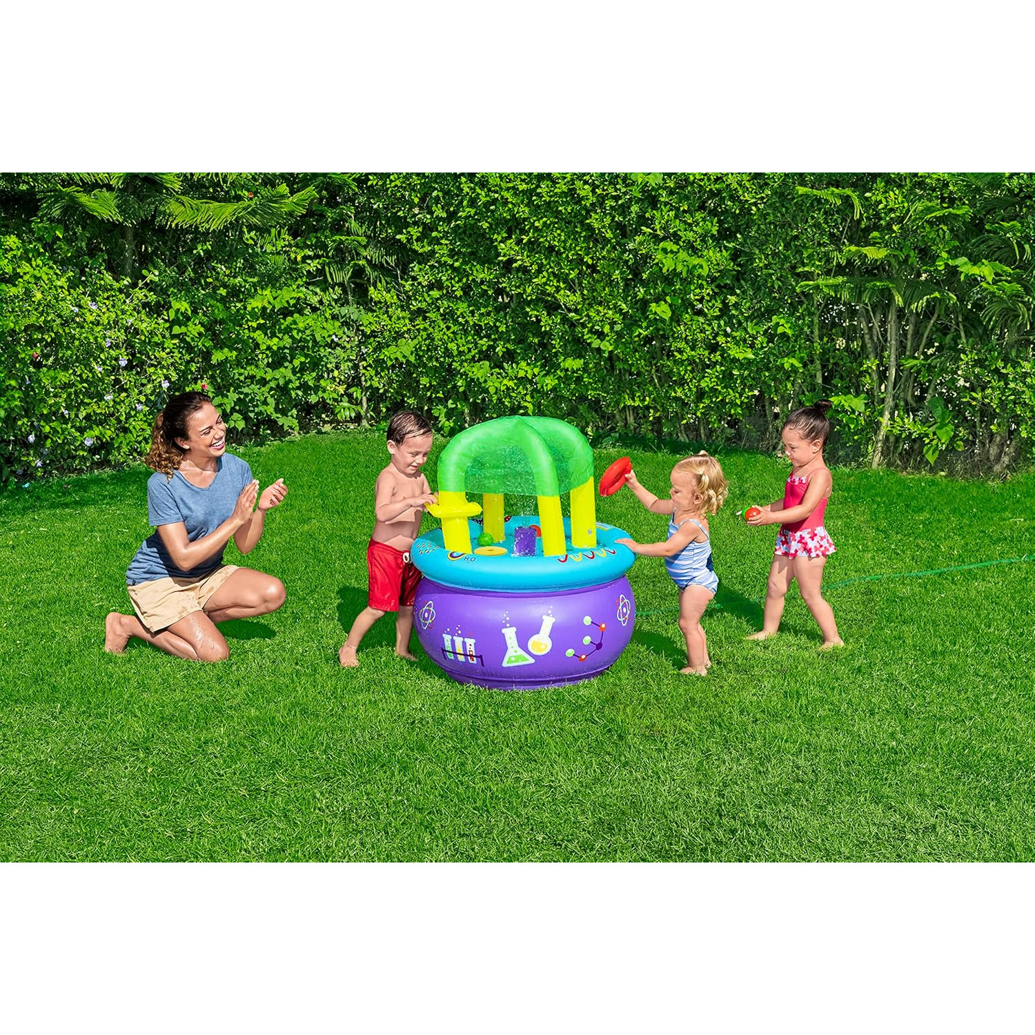 Bambini e una donna giocano con l'acqua in giardino. Usano una piscina gonfiabile viola con un arco verde, sull'erba verde.