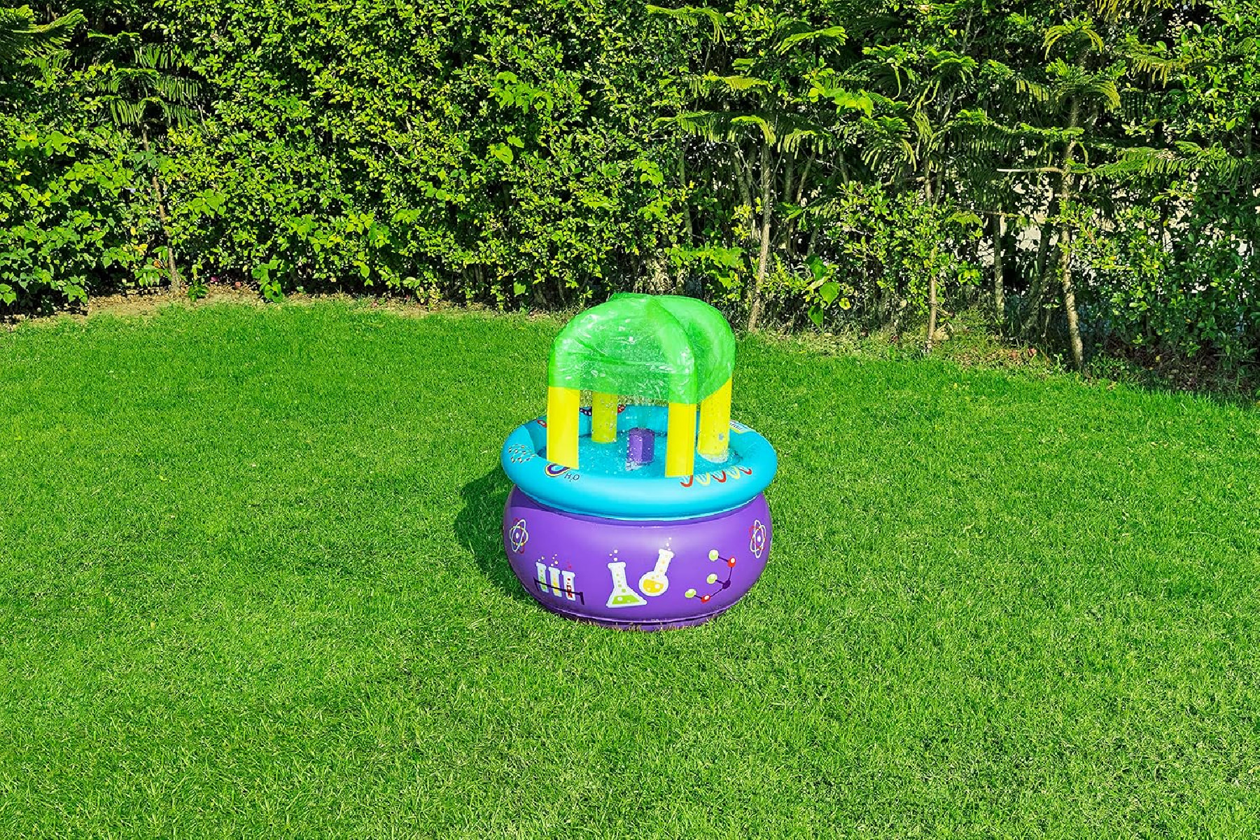 Un gioco d'acqua gonfiabile viola e blu su un prato, con una tettoia verde. Una siepe verde sullo sfondo.