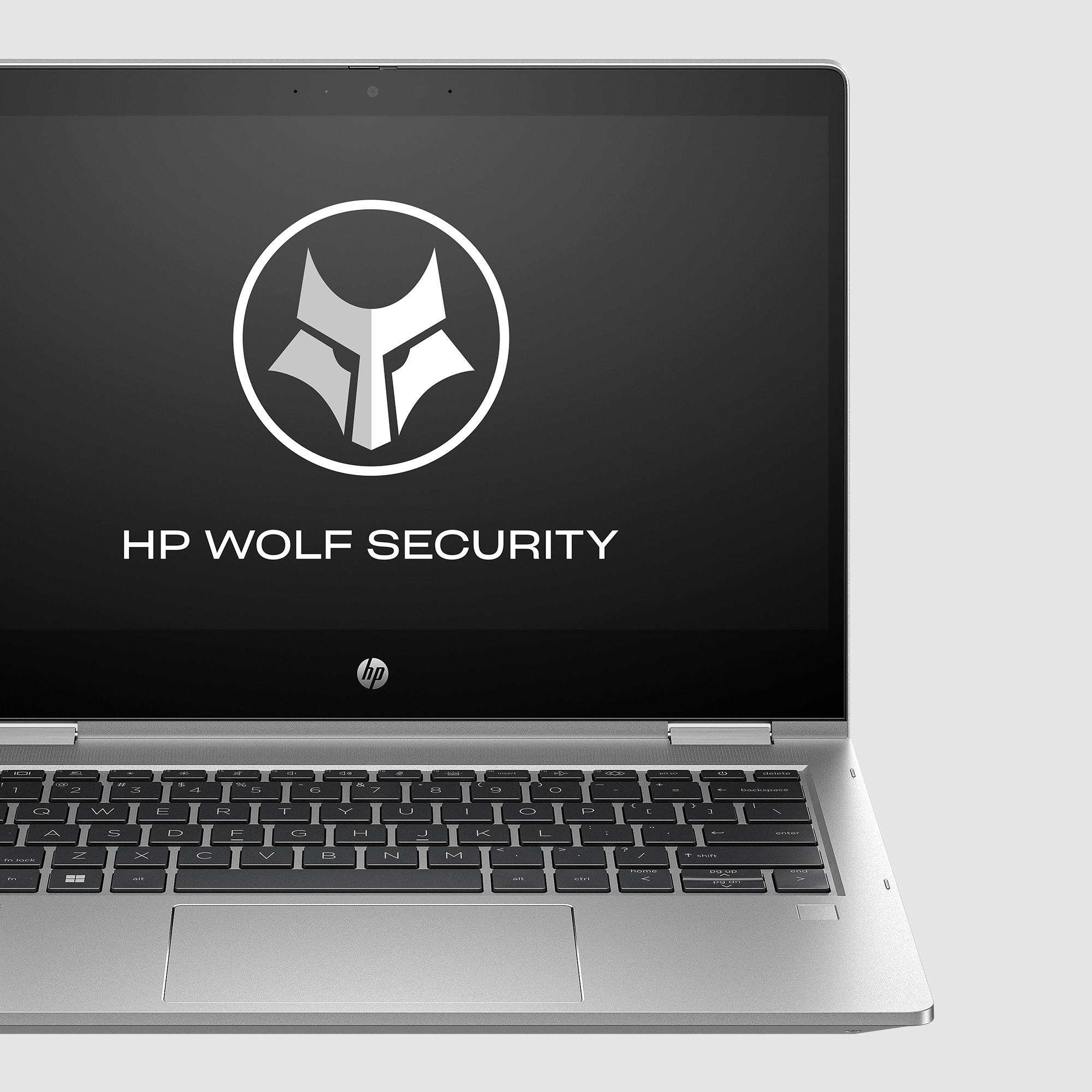 Laptop z logo HP Wolf Security na ekranie. Srebrna klawiatura i jasnoszare tło.