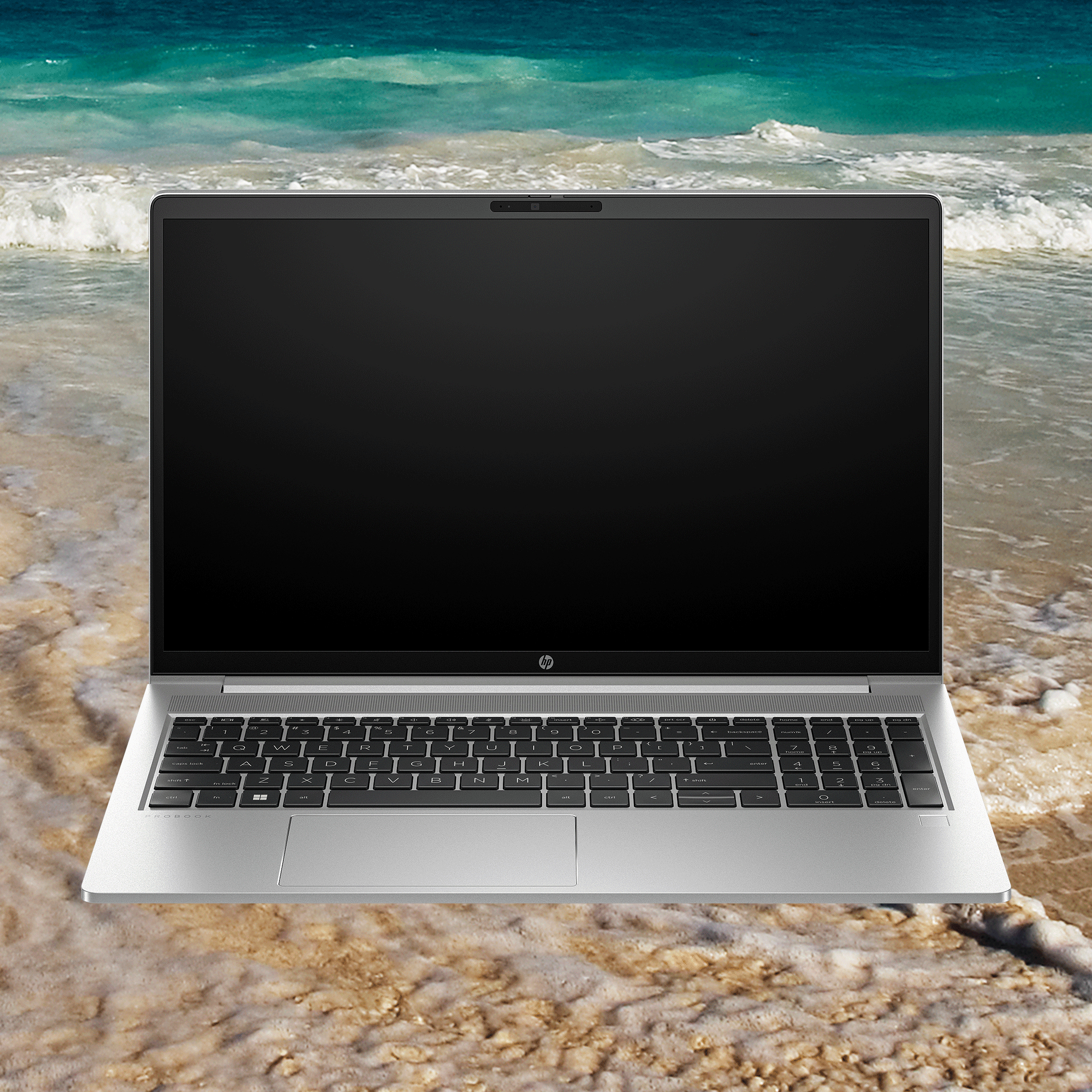 Laptop HP plateado en una playa. La pantalla es negra, olas y arena en el fondo.