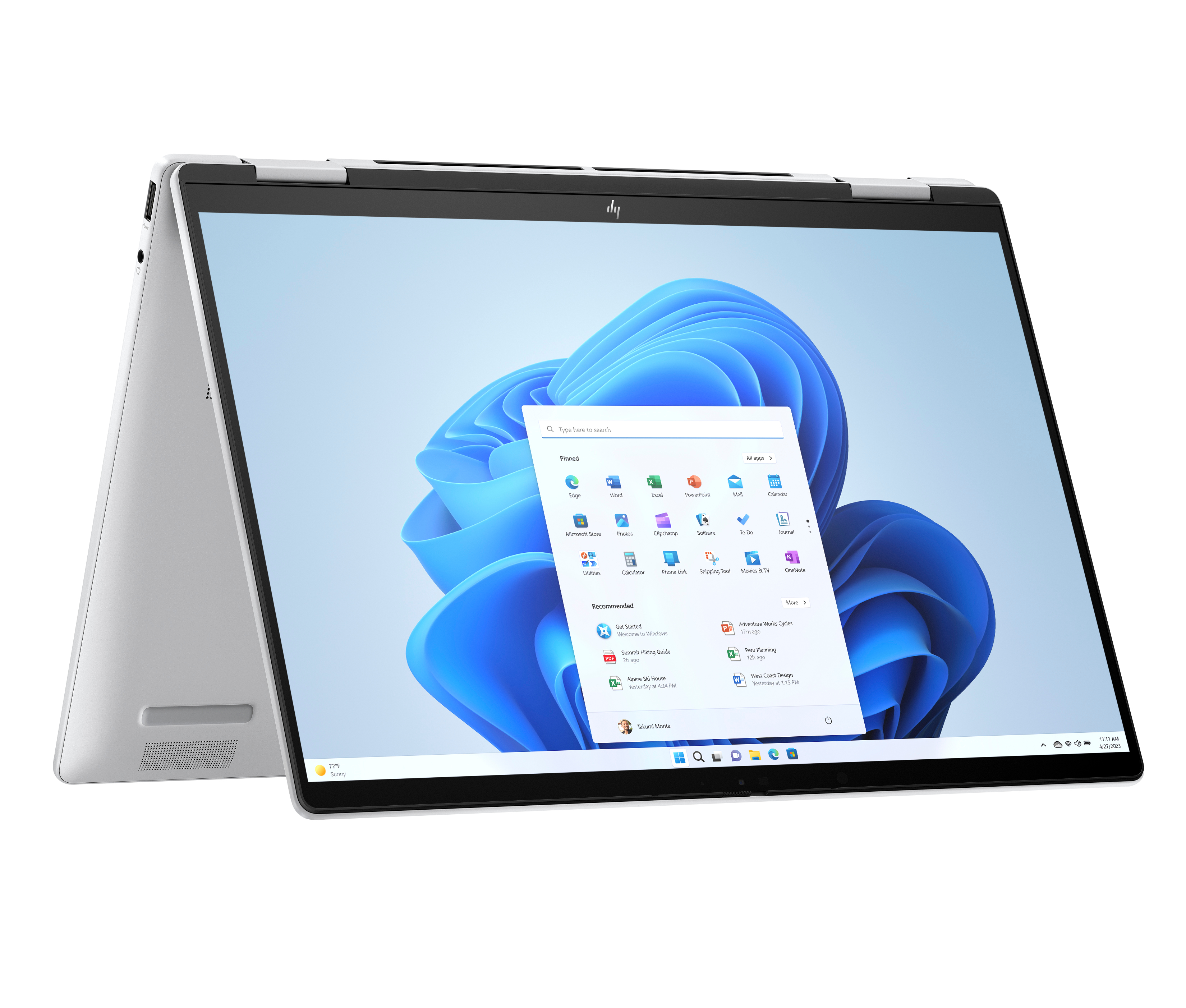 Srebrny laptop z interfejsem Windows 11. Ekran wyświetla ikony aplikacji i pasek wyszukiwania. Urządzenie jest otwarte i pod kątem.