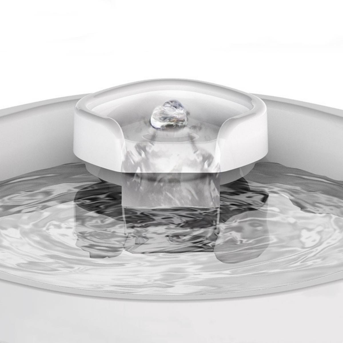 Ein weißer Trinkbrunnen für Haustiere. Wasser fließt aus einem zentralen Auslauf in eine Schüssel. Das Wasser ist klar und der Brunnen ist weiß.