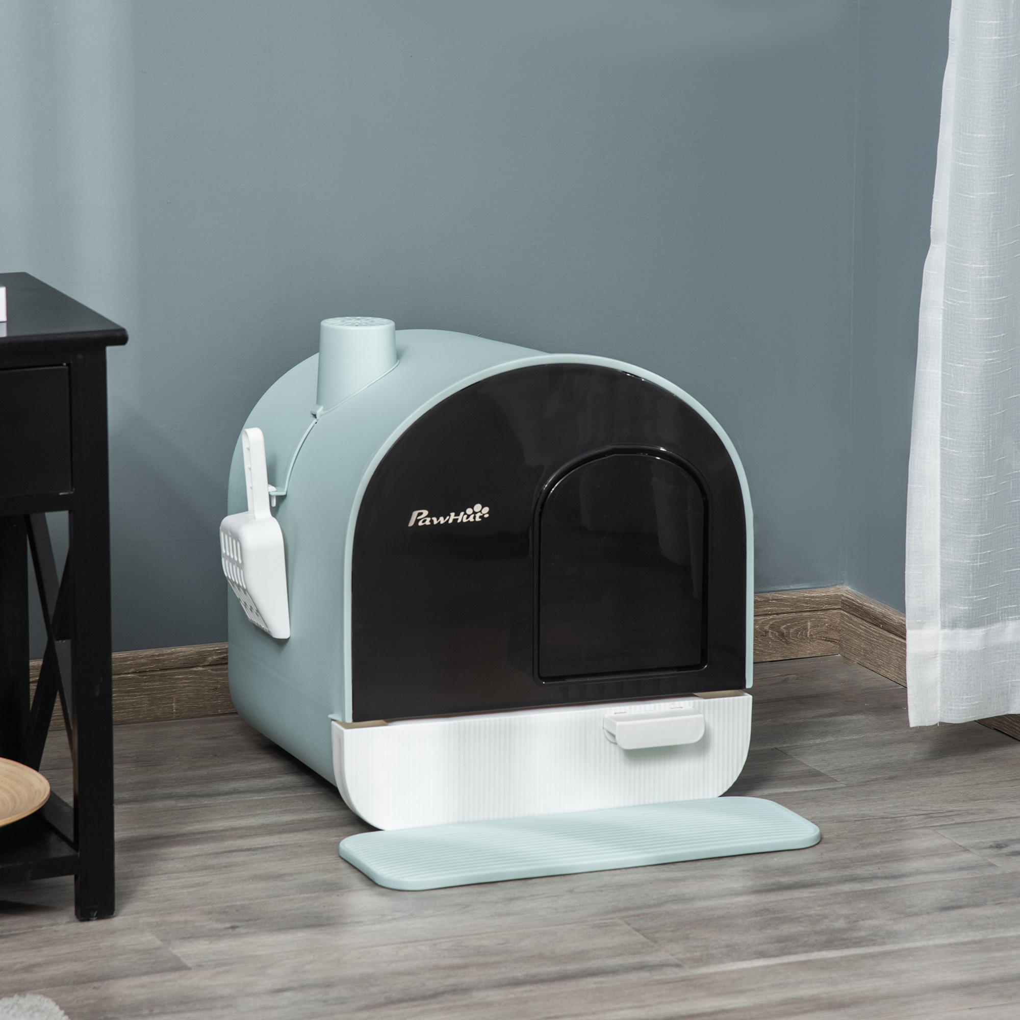 Eine Katzentoilette, hellblau und schwarz, mit einer Schaufel, steht auf einem Holzboden in der Nähe eines Beistelltisches und eines Vorhangs.