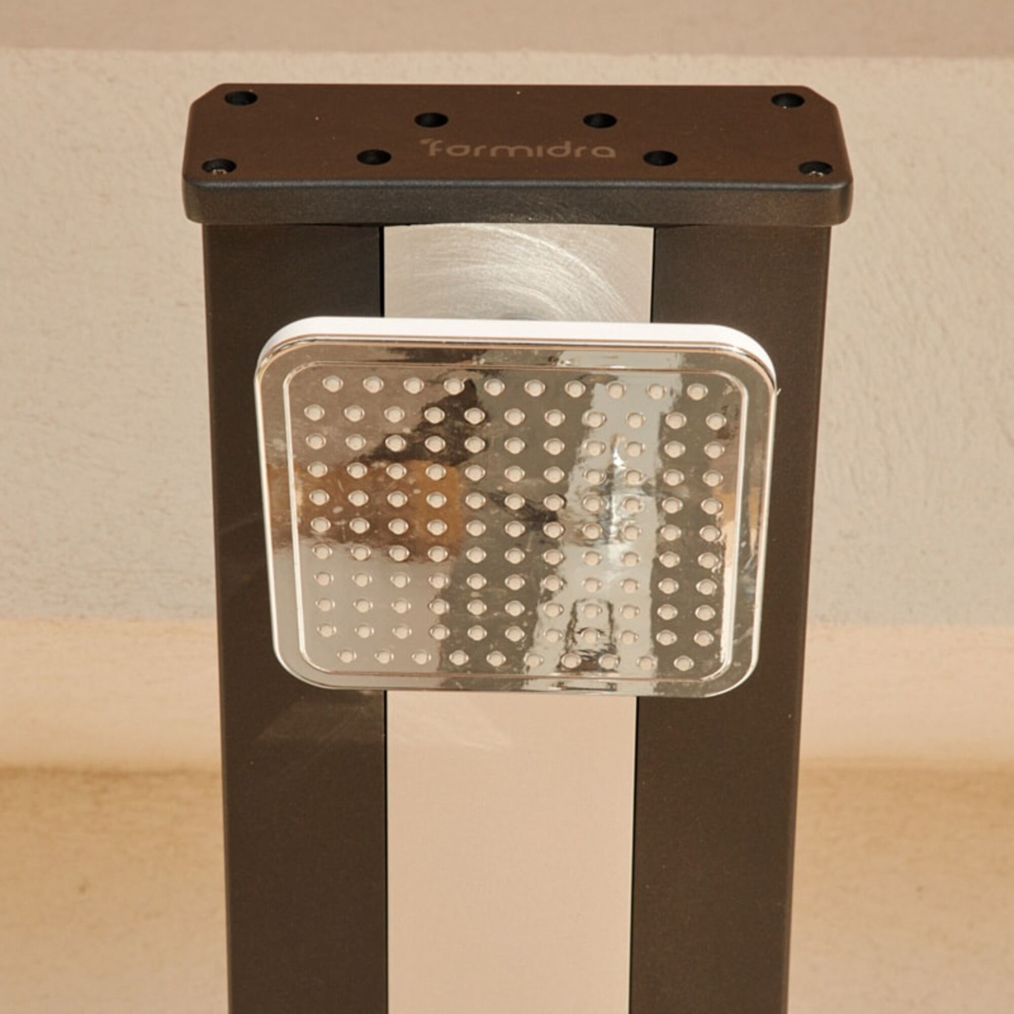 Una columna de ducha de metal negro con un cabezal de ducha cuadrado. El fondo es una pared beige.