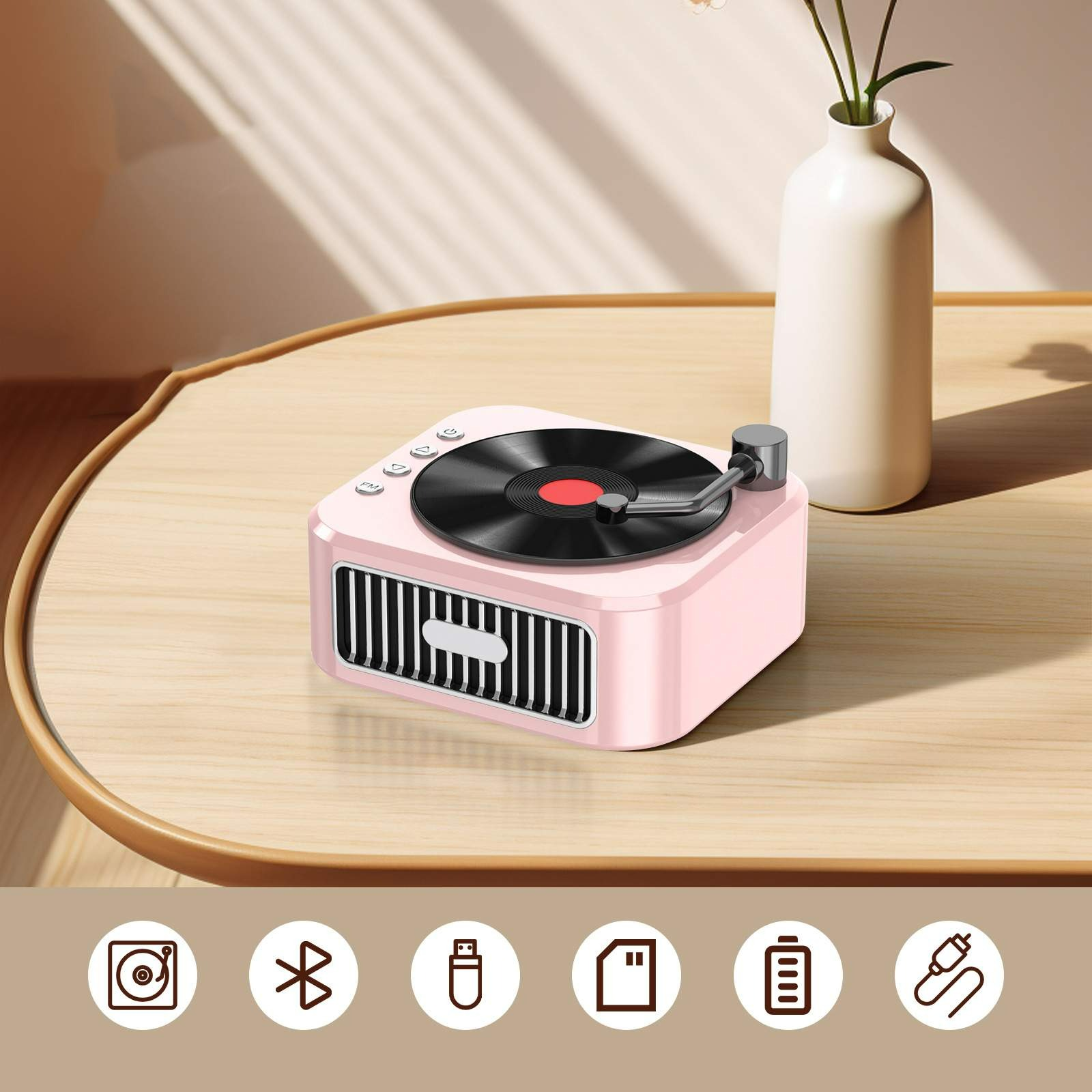 Rosa Retro-Lautsprecher mit Plattenspieler-Design auf einem Holztisch mit einer Vase. Konnektivitäts-Icons sind unten.