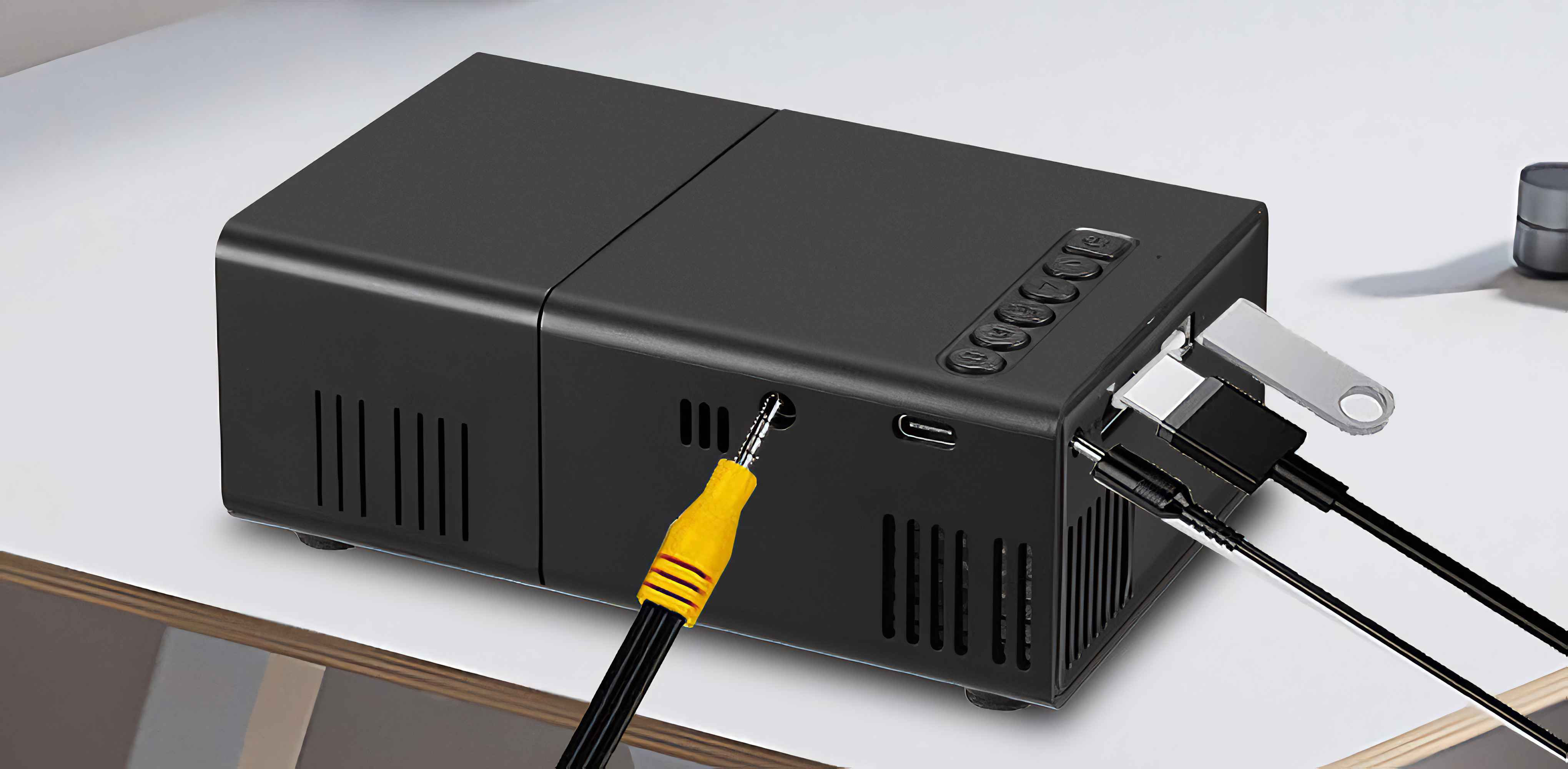 Ein schwarzer Projektor mit Kabeln und einem USB-Stick. Ein gelb-schwarzes Audiokabel ist angeschlossen.