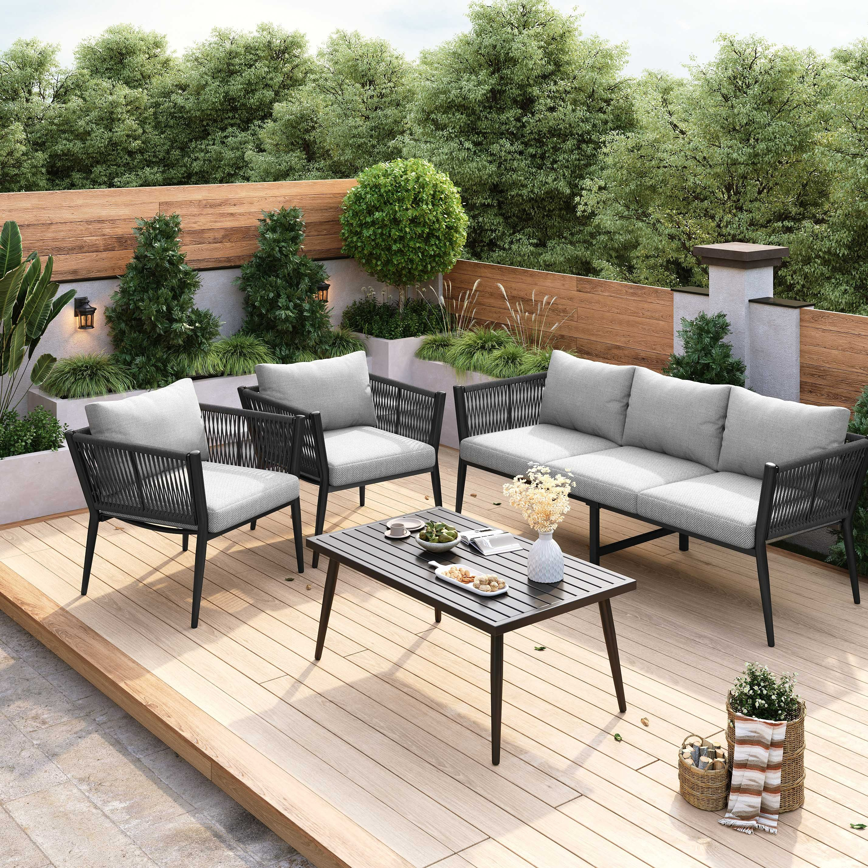 Terrasse mit grauen Sitzmöbeln, Tisch mit Snacks und Pflanzen. Holzterrasse mit natürlichem Baumhintergrund.