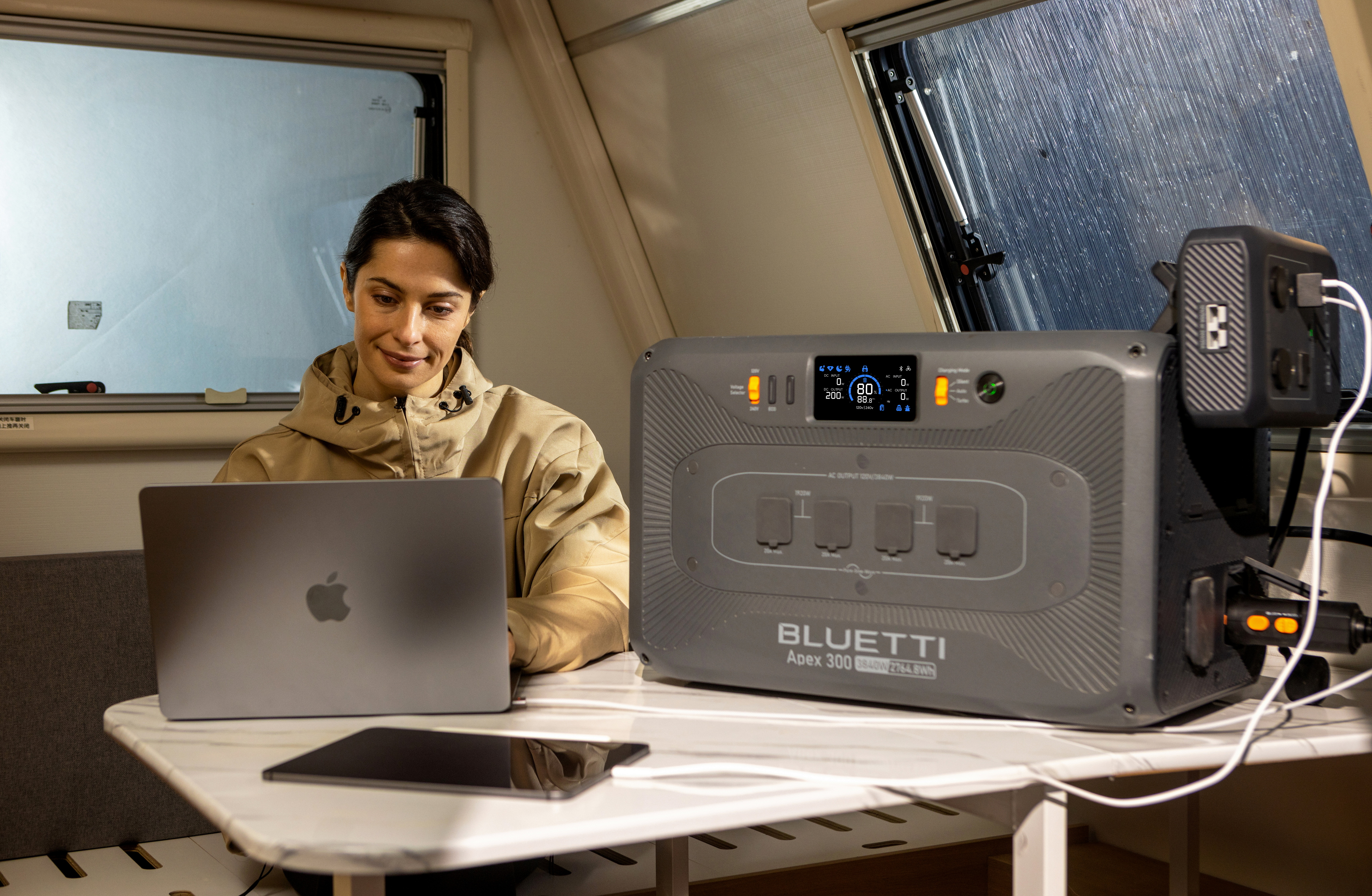 Kobieta używa laptopa w kamperze. Stacja zasilania stoi na stole, ładując urządzenia. Okno jest za nią.