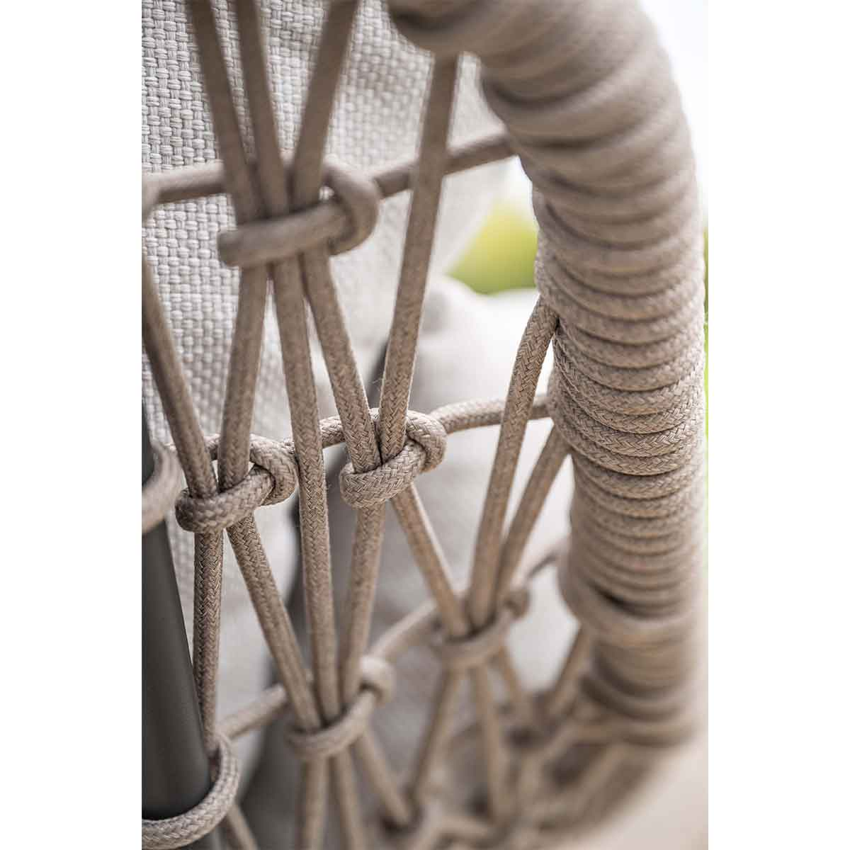 Close-up van een geweven rugleuning. Beige touwen zijn geknoopt om de structuur te vormen. Een grijze stof is zichtbaar achter de touwen.