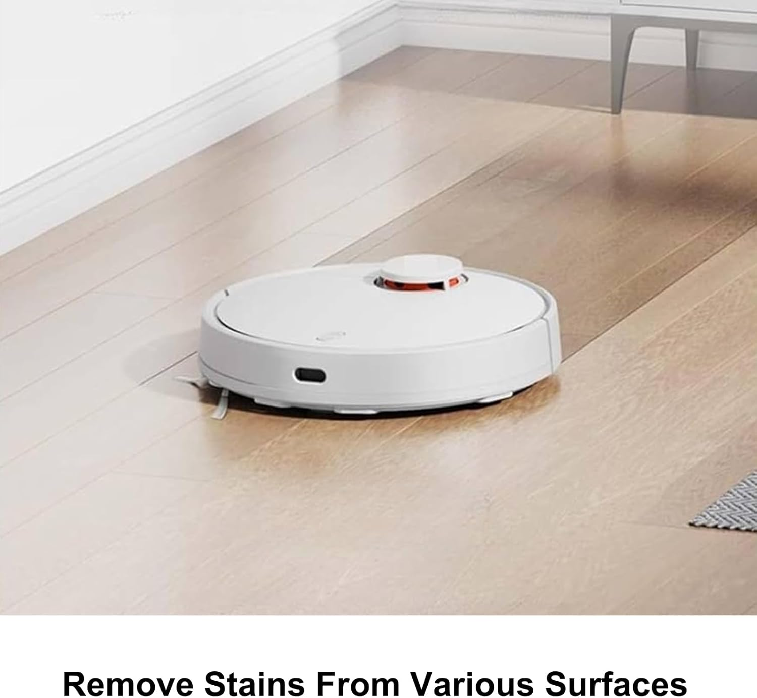 Ein weißer Roboterstaubsauger auf einem Holzboden. Der Staubsauger ist kreisförmig mit roter Oberseite. Der Hintergrund zeigt eine weiße Wand.