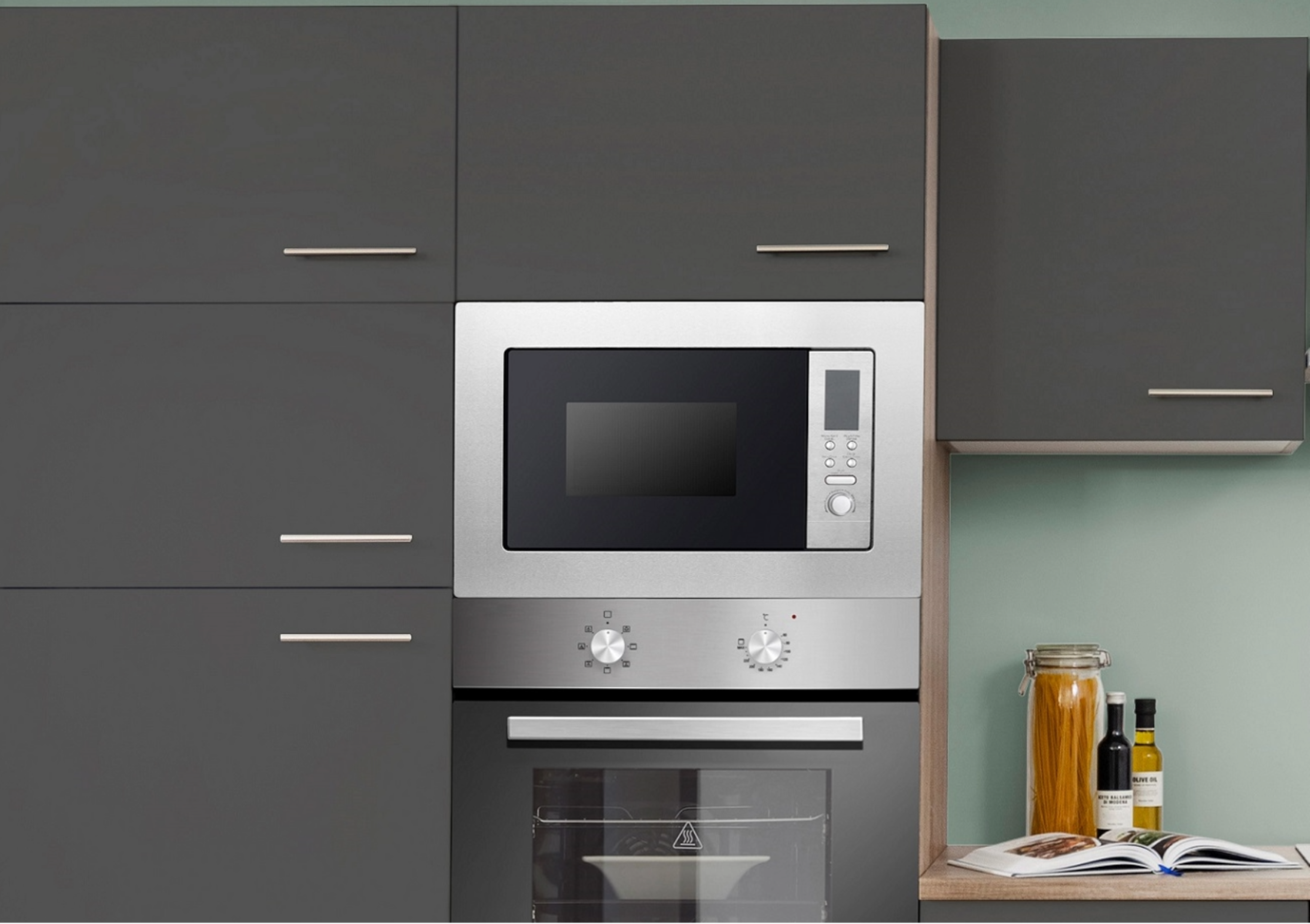 A kitchen with a microwave, oven, and cabinets. A jar of pasta, oil bottles, and a cookbook are also visible.