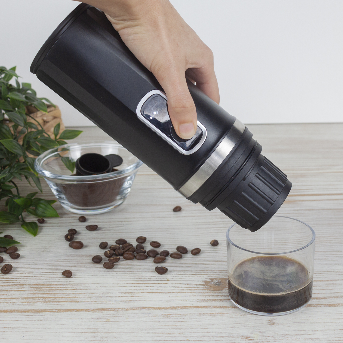 Ręka naciska przycisk na czarnym ekspresie do kawy, nalewając kawę do szklanki. Widoczne są ziarna i zmielona kawa.