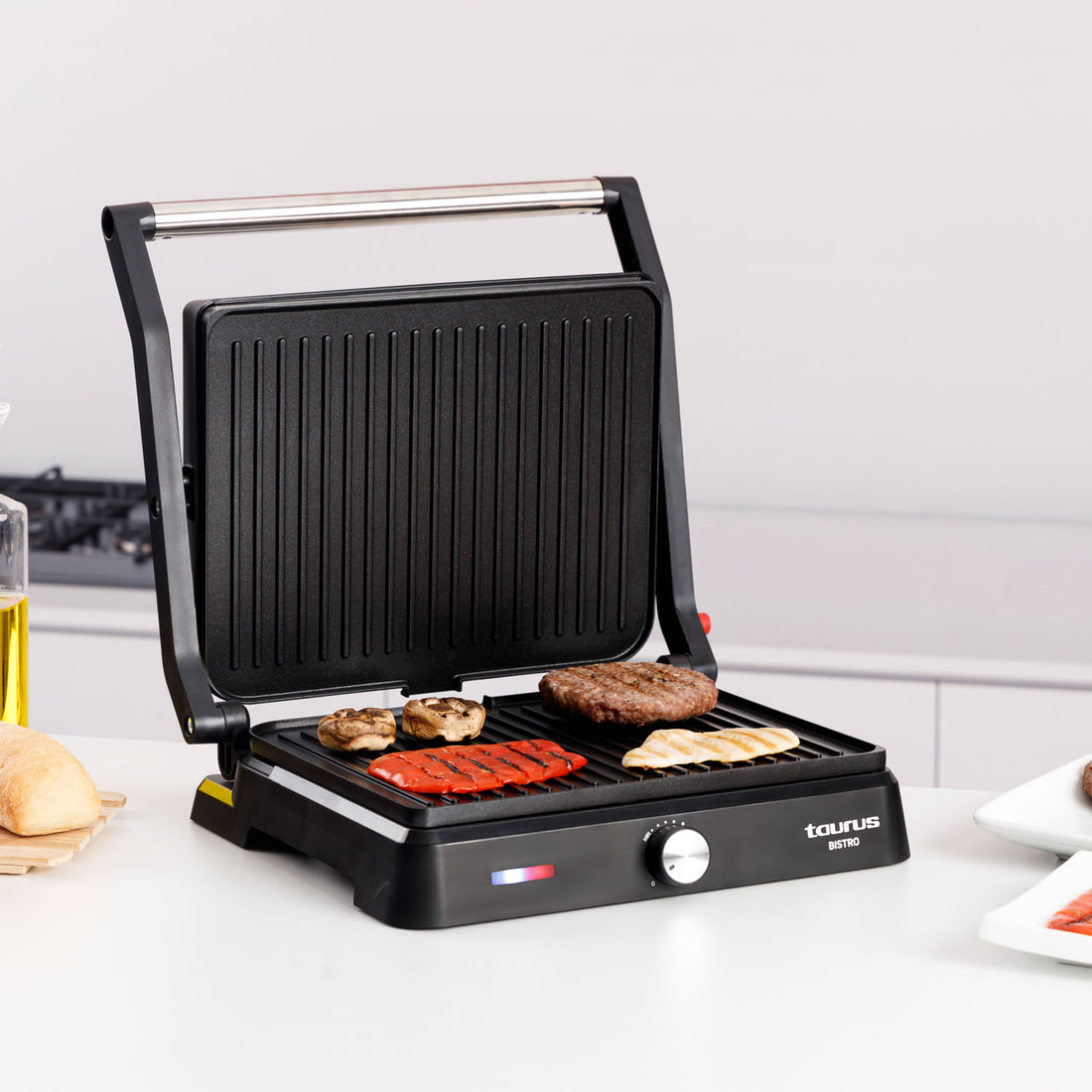 Una griglia nera con cibo: hamburger, peperone, funghi e pollo. La griglia è su una superficie bianca. Lo sfondo è una cucina bianca.