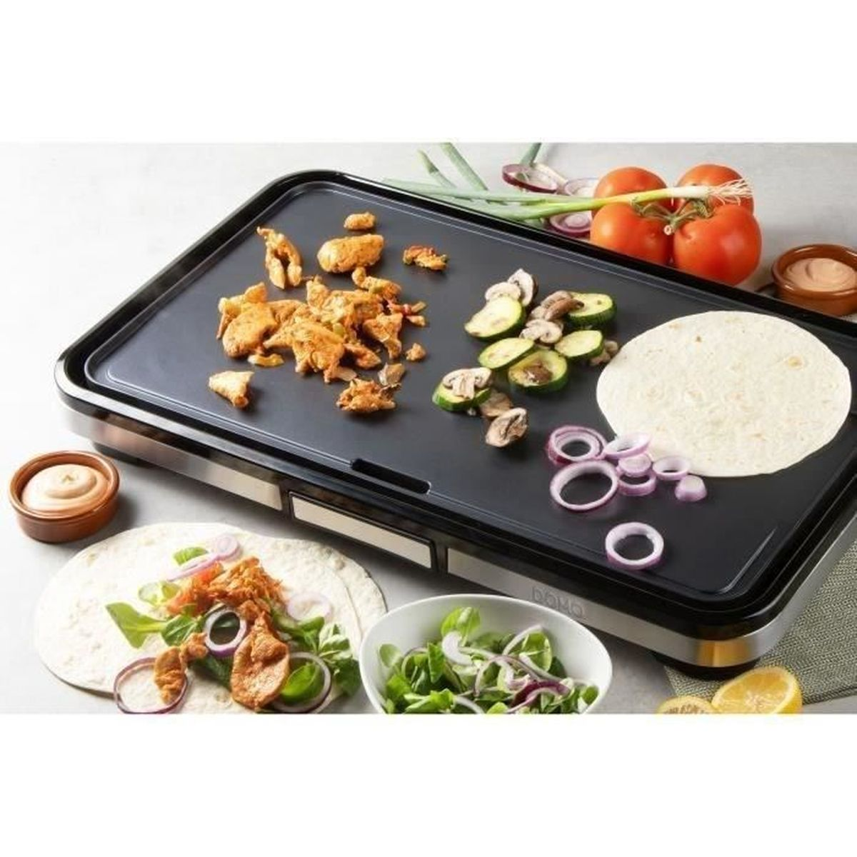 Ein Grill mit Hähnchen, Gemüse und Tortillas. Tomaten, Zwiebeln und Saucen stehen daneben. Eine Wrap wird zubereitet.