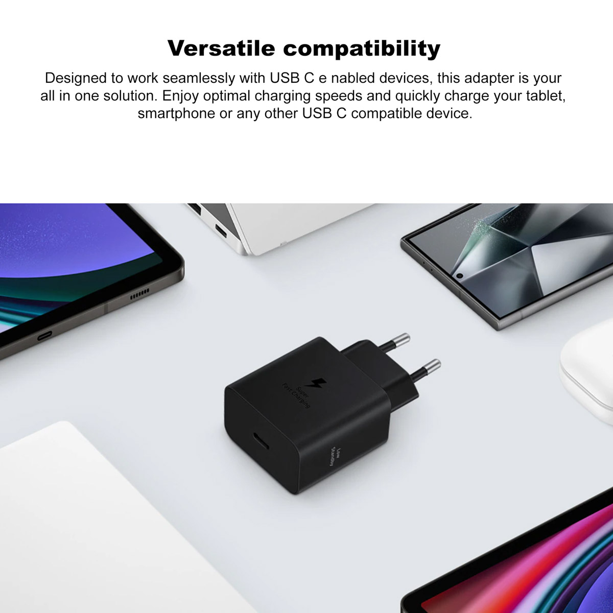 Un cargador USB-C negro con clavijas plateadas está rodeado de dispositivos electrónicos, como una tableta y un teléfono inteligente.