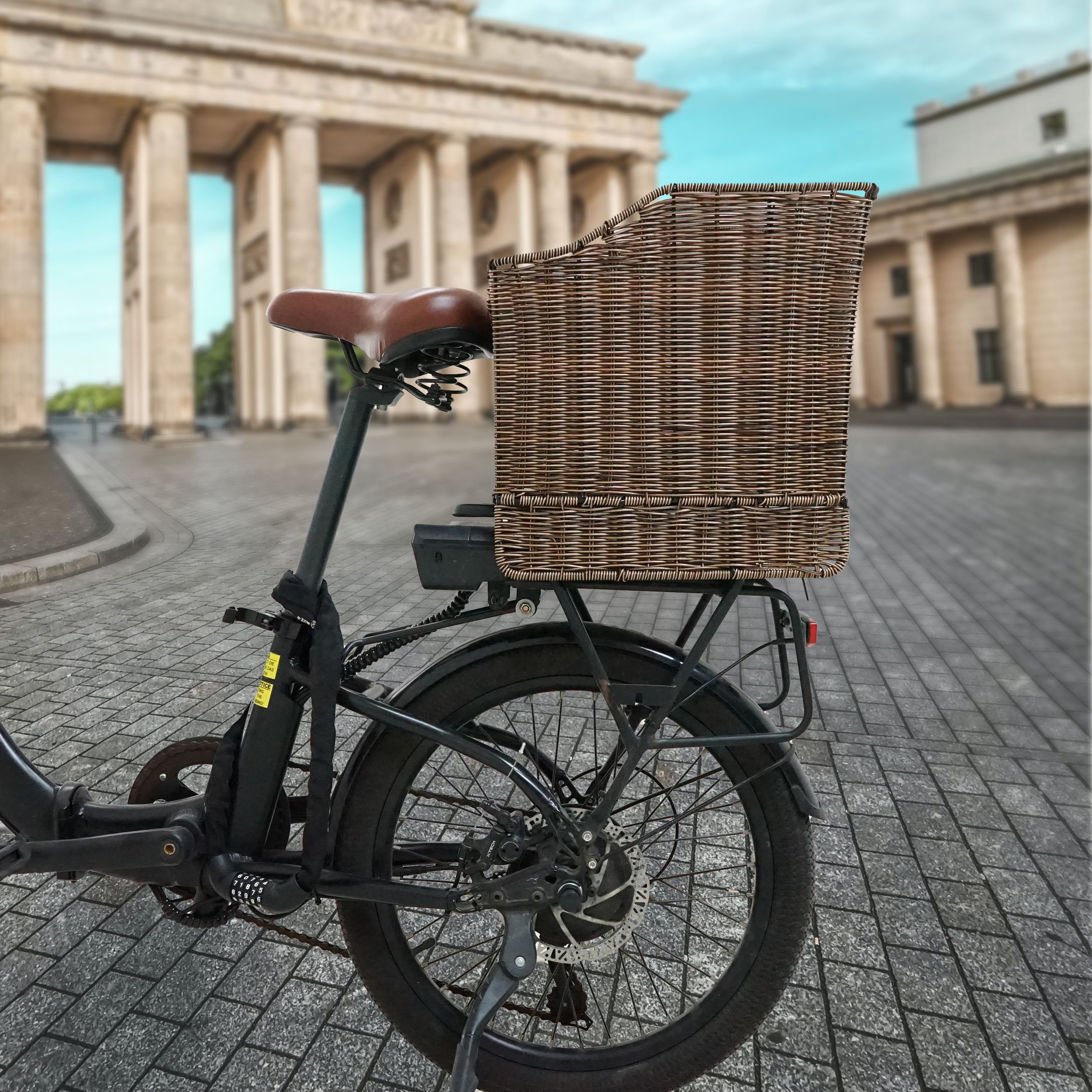 Ein Fahrrad mit Korb vor dem Brandenburger Tor. Das Fahrrad ist schwarz mit braunem Sattel, der Korb ist braun.