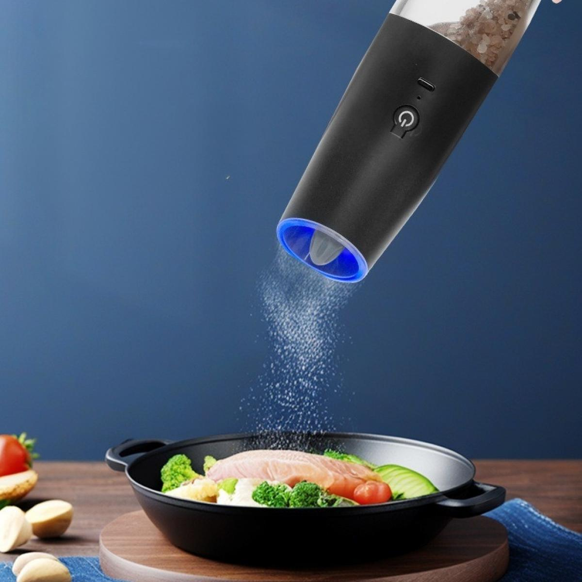 Ein schwarzer elektrischer Grinder streut Salz auf eine Pfanne mit Essen, darunter Lachs und Gemüse, auf einer Holzoberfläche.