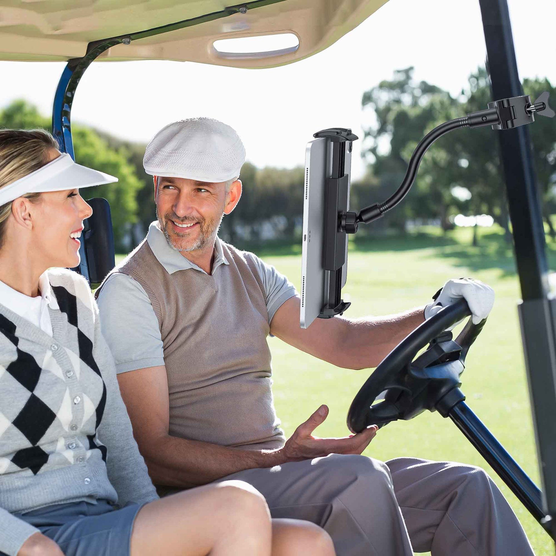 Para w wózku golfowym, mężczyzna prowadzi, kobieta się uśmiecha, uchwyt na tablet. Zielone tło pola golfowego.