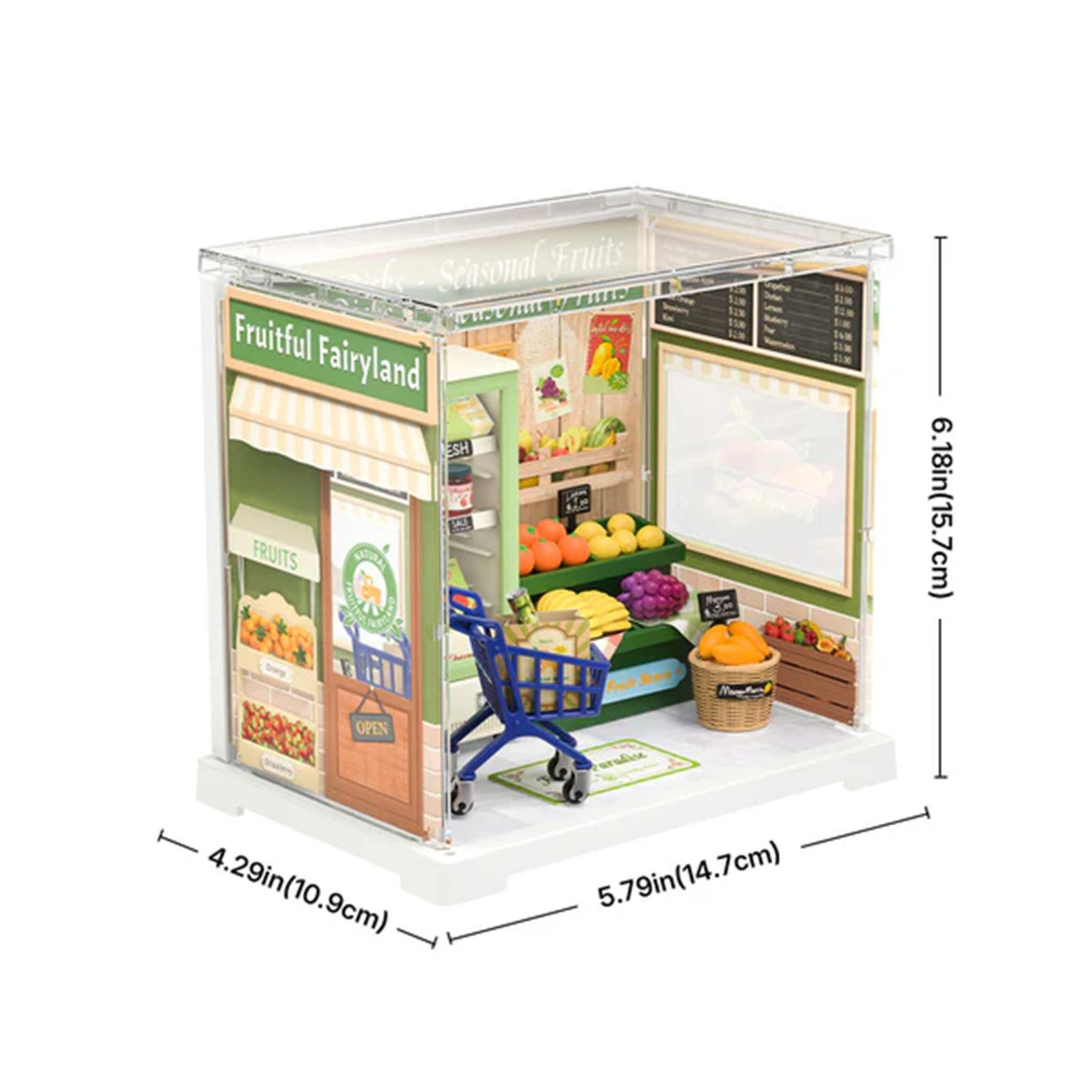Miniatur-Obstladen mit blauem Einkaufswagen und verschiedenen Früchten. Der Laden trägt die Aufschrift 'Fruitful Fairyland'.