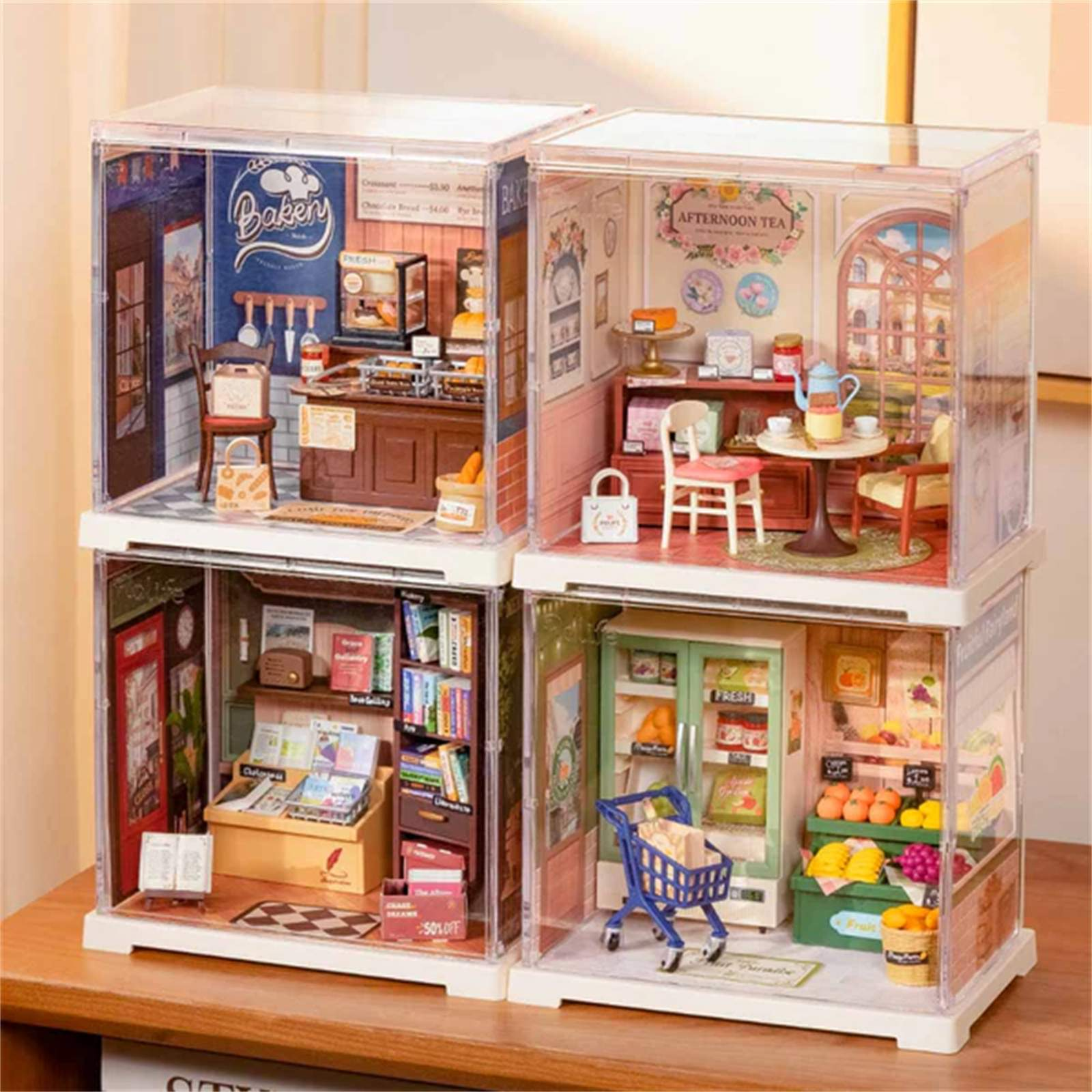 Miniatur-Läden in durchsichtigen Boxen: Bäckerei, Teestube, Buchhandlung und Obstladen, mit detaillierten Innenräumen.