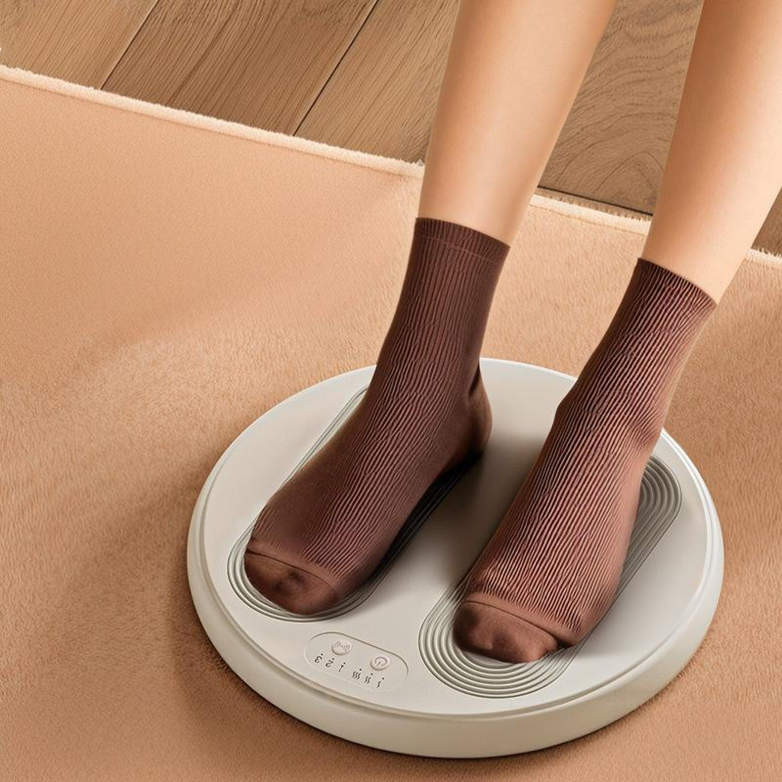 Füße in braunen Socken auf einem Fußmassagegerät. Beiger Teppich und Holzboden im Hintergrund.