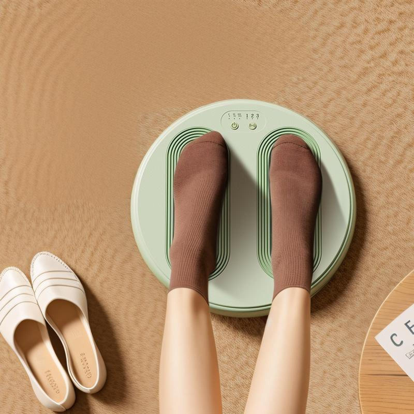Füße in braunen Socken auf einem Fußmassagegerät. Weiße Schuhe und ein Tisch mit einer Zeitschrift sind im Bild.