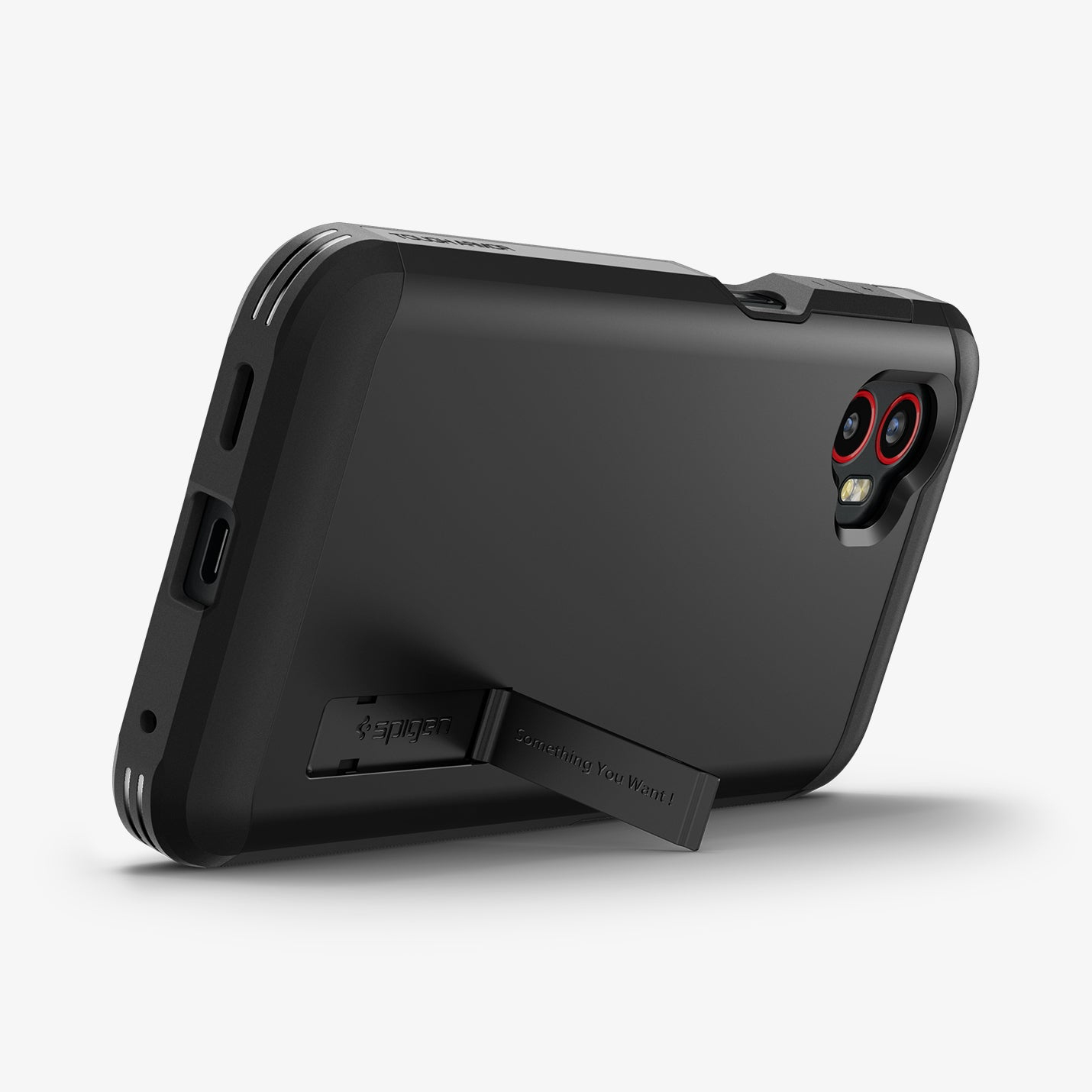 Black phone case with a kickstand, resting on a white surface. The case has the Spigen logo and a camera cutout.