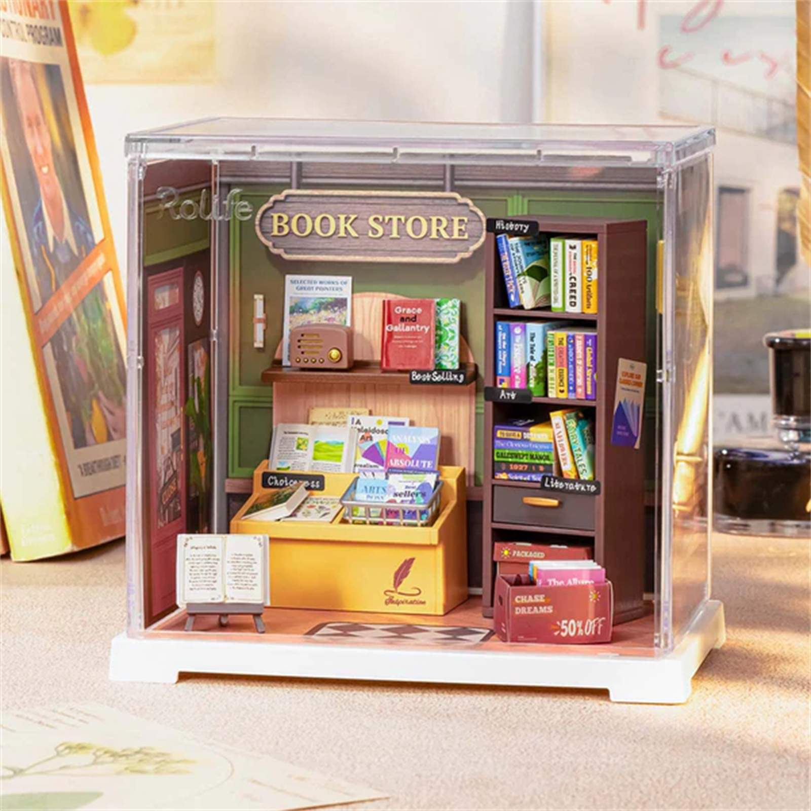 Ein Miniatur-Buchladendiorama mit Büchern, Regalen und einem Schild. Bücher werden ausgestellt. Die Szene befindet sich in einer transparenten Vitrine.