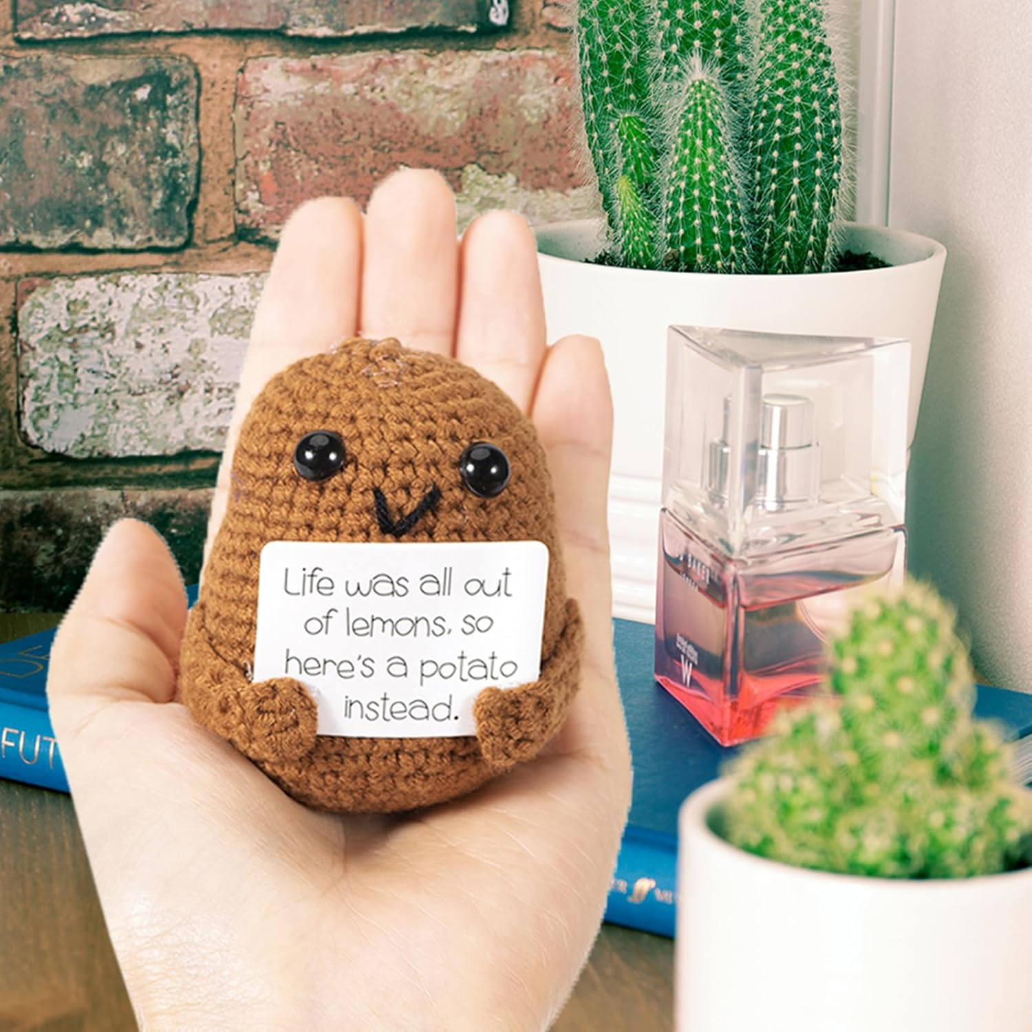 Eine Hand hält eine gehäkelte Kartoffel, die ein Schild mit der Aufschrift "Life was all out of lemons, so here's a potato instead." hält.