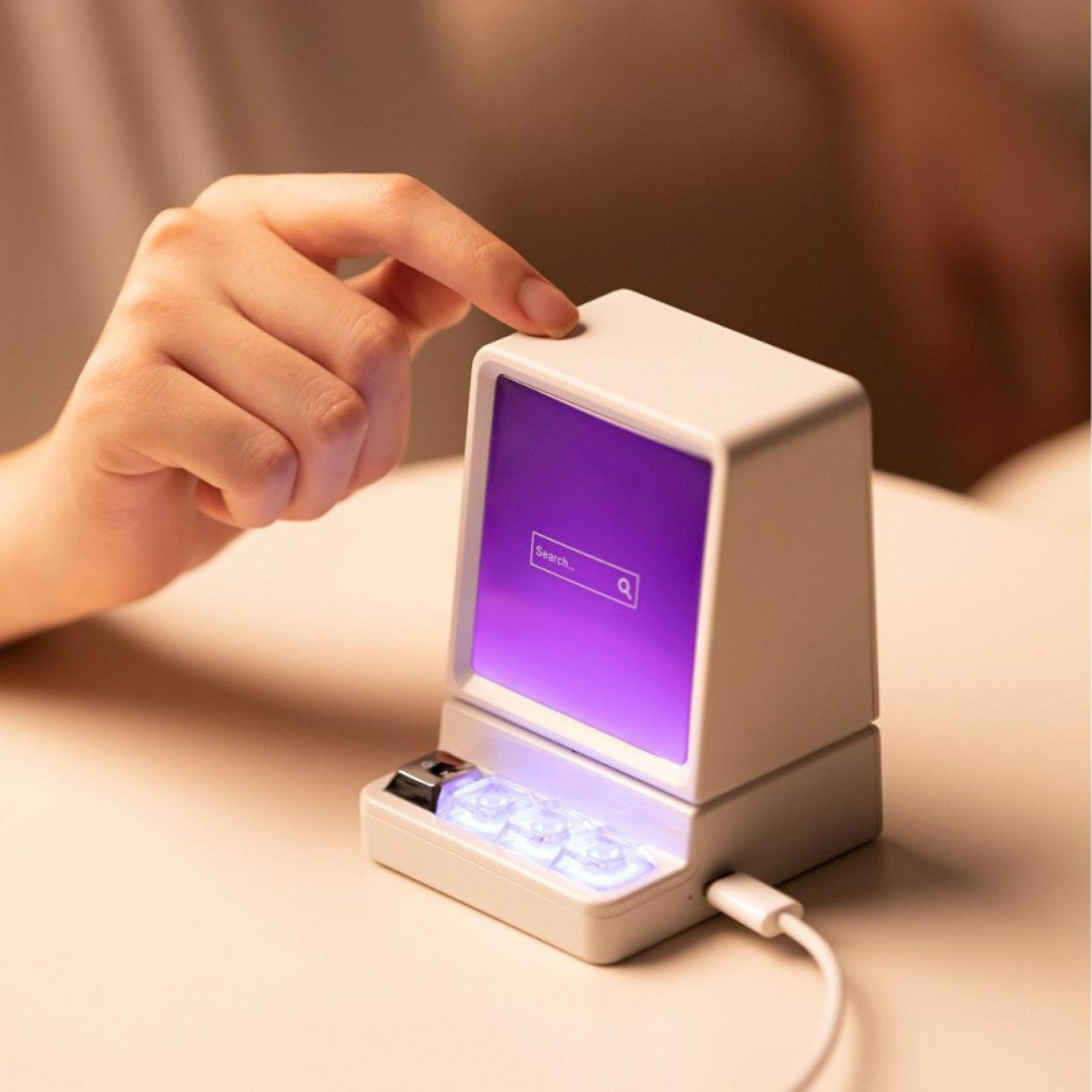 Hand berührt einen kleinen weißen Retro-Computer. Der Bildschirm zeigt einen lila Farbton und eine Suchleiste.