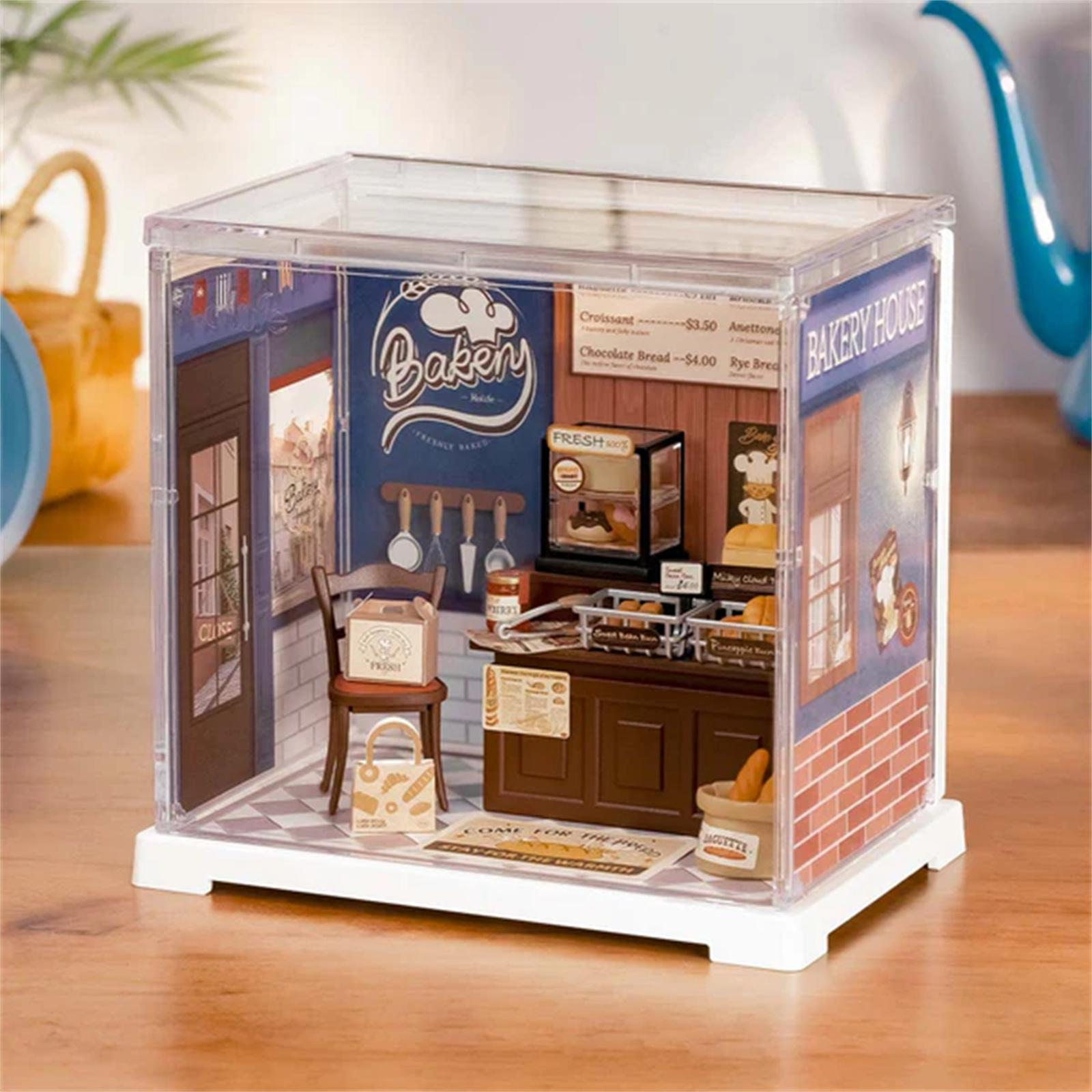 Eine Miniatur-Bäckerei-Szene in einer transparenten Box. Mit Theke, Backwaren, Stuhl und Tür.