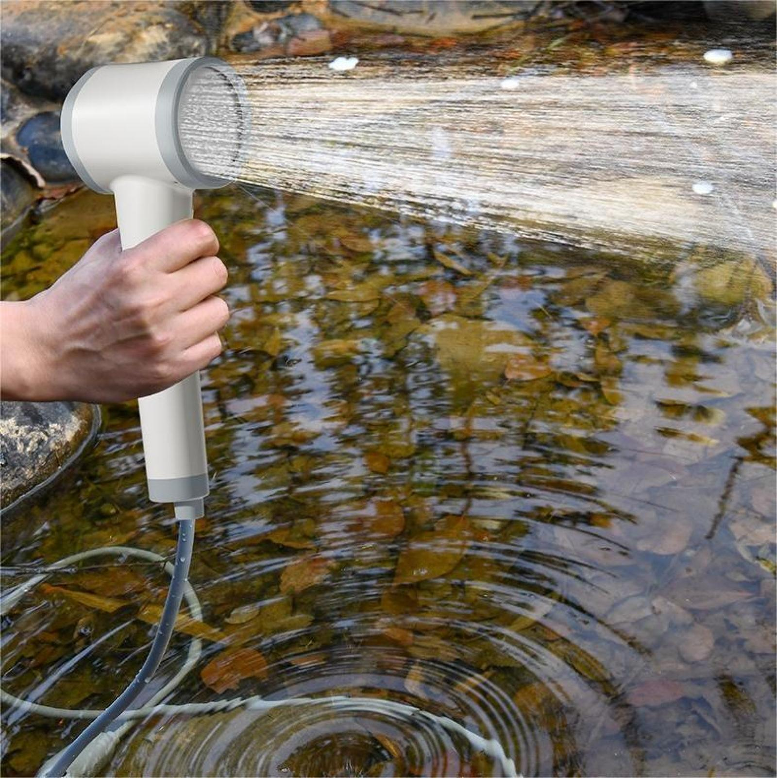 Eine Hand hält einen weißen Duschkopf, der Wasser in einen Bach mit Herbstlaub sprüht.